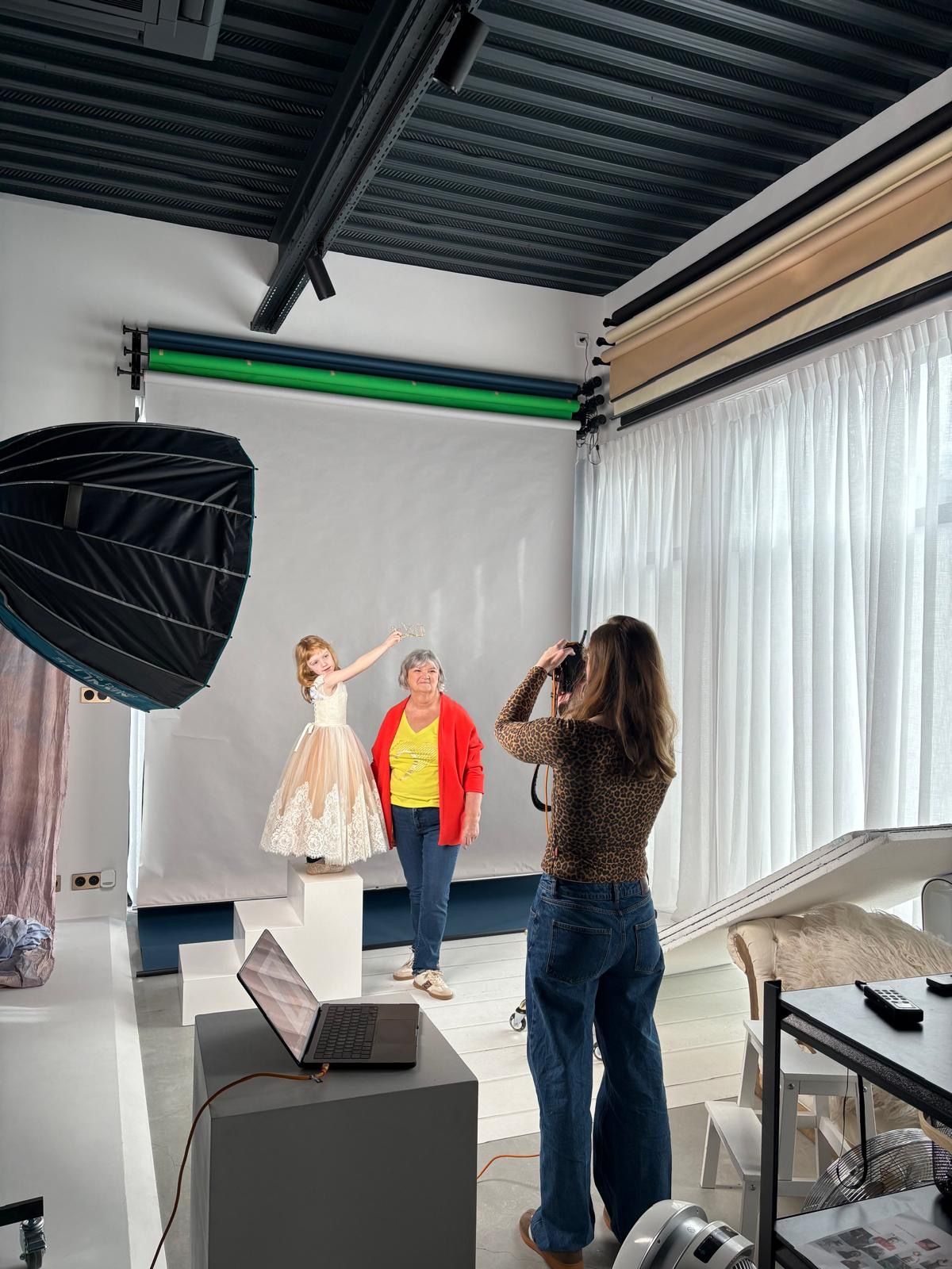 Photographer shooting grandmother and young girl in elegant dress in professional studio.