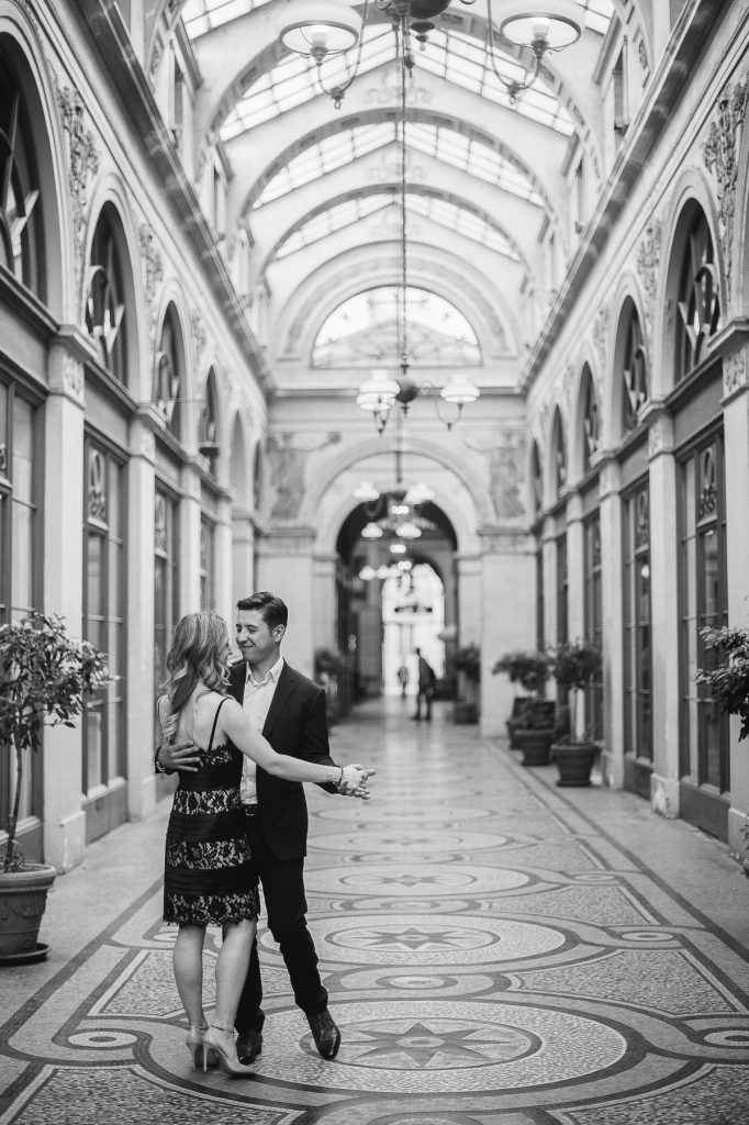 Black and white romantic photo of a couple dancing together in the grand arcade of Galerie Vivienne, Paris.