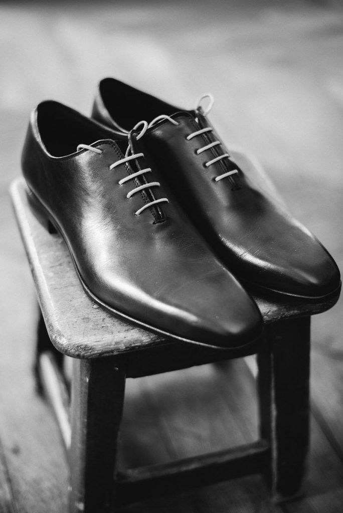 Classic black leather Oxford dress shoes displayed on a wooden stool in black and white photo.