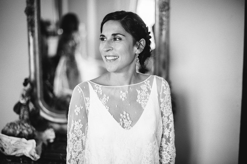 Black and white portrait of smiling bride in lace wedding dress near ornate gold mirror.