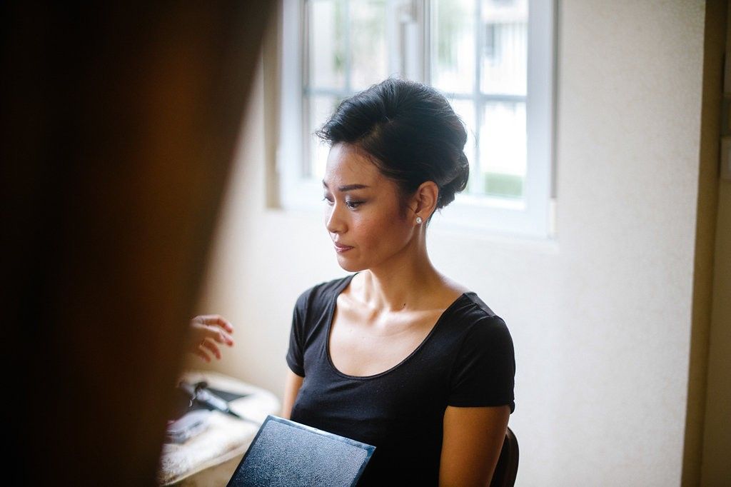 Elegant woman with updo hairstyle holding a portfolio near a bright window indoors.