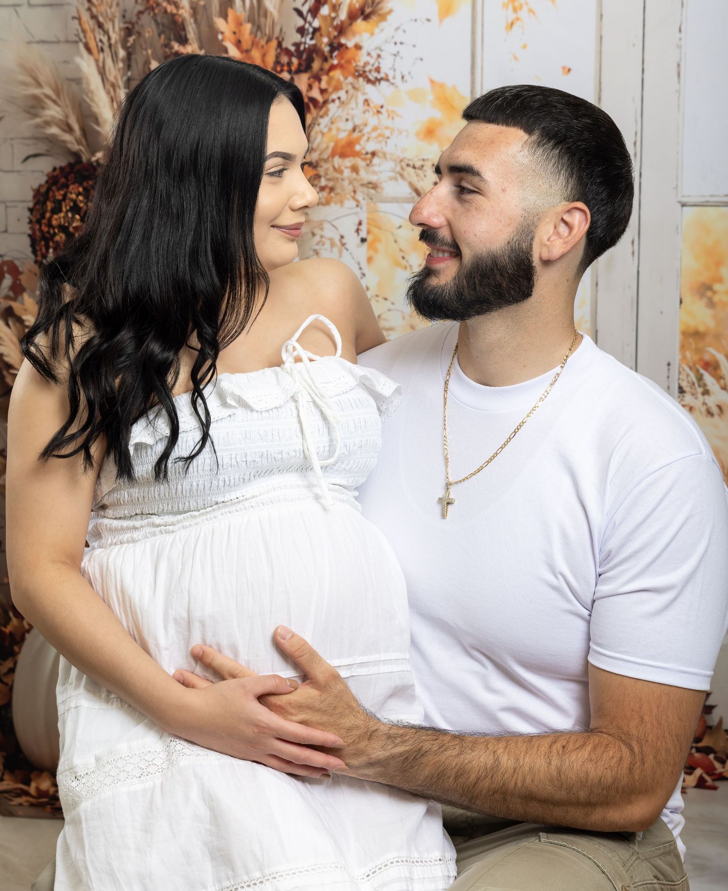 Couple in white outfits sharing a tender maternity photo moment, man gently holding pregnant woman's belly.