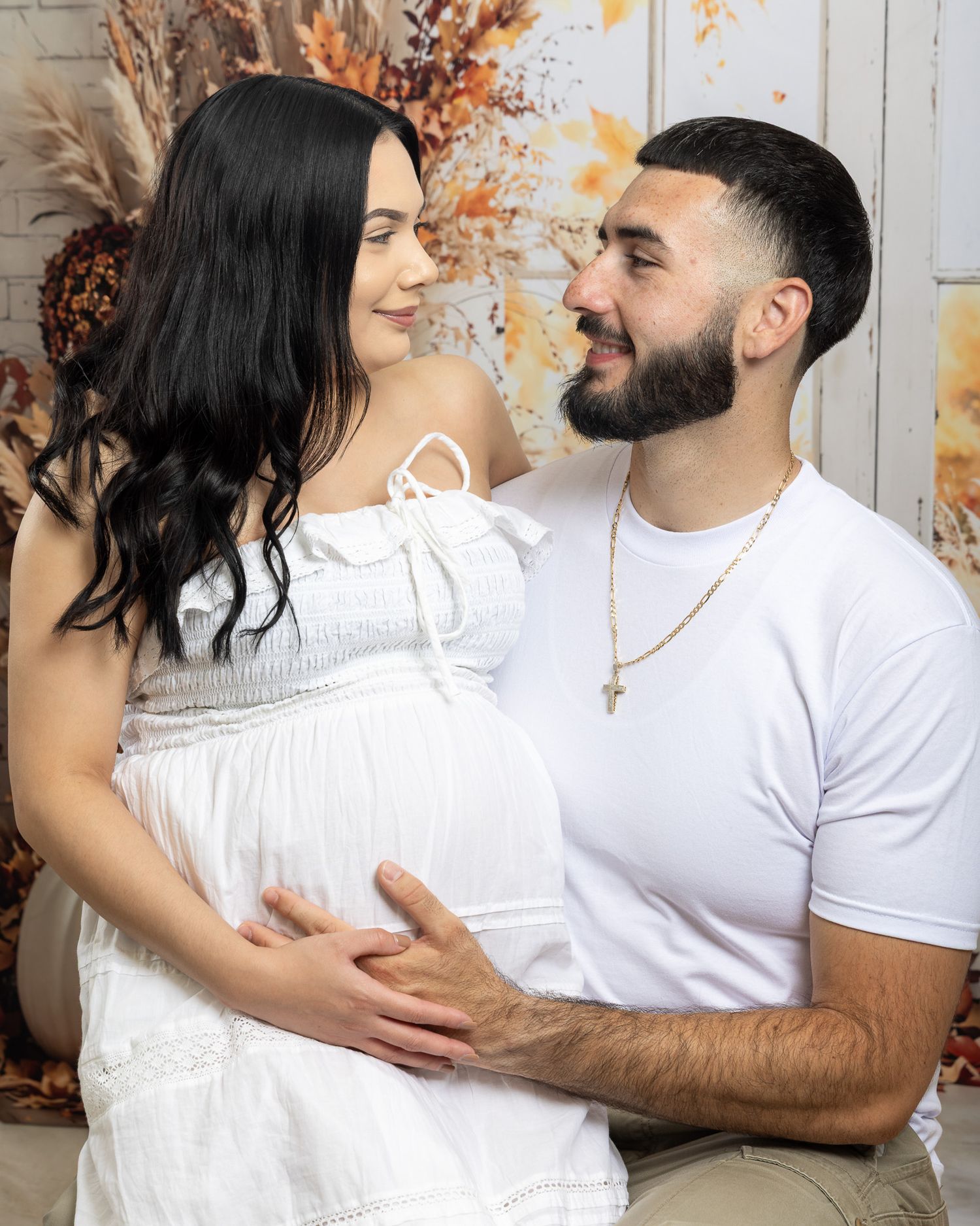 Couple in white outfits sharing a tender maternity photo moment, man gently holding pregnant woman's belly.