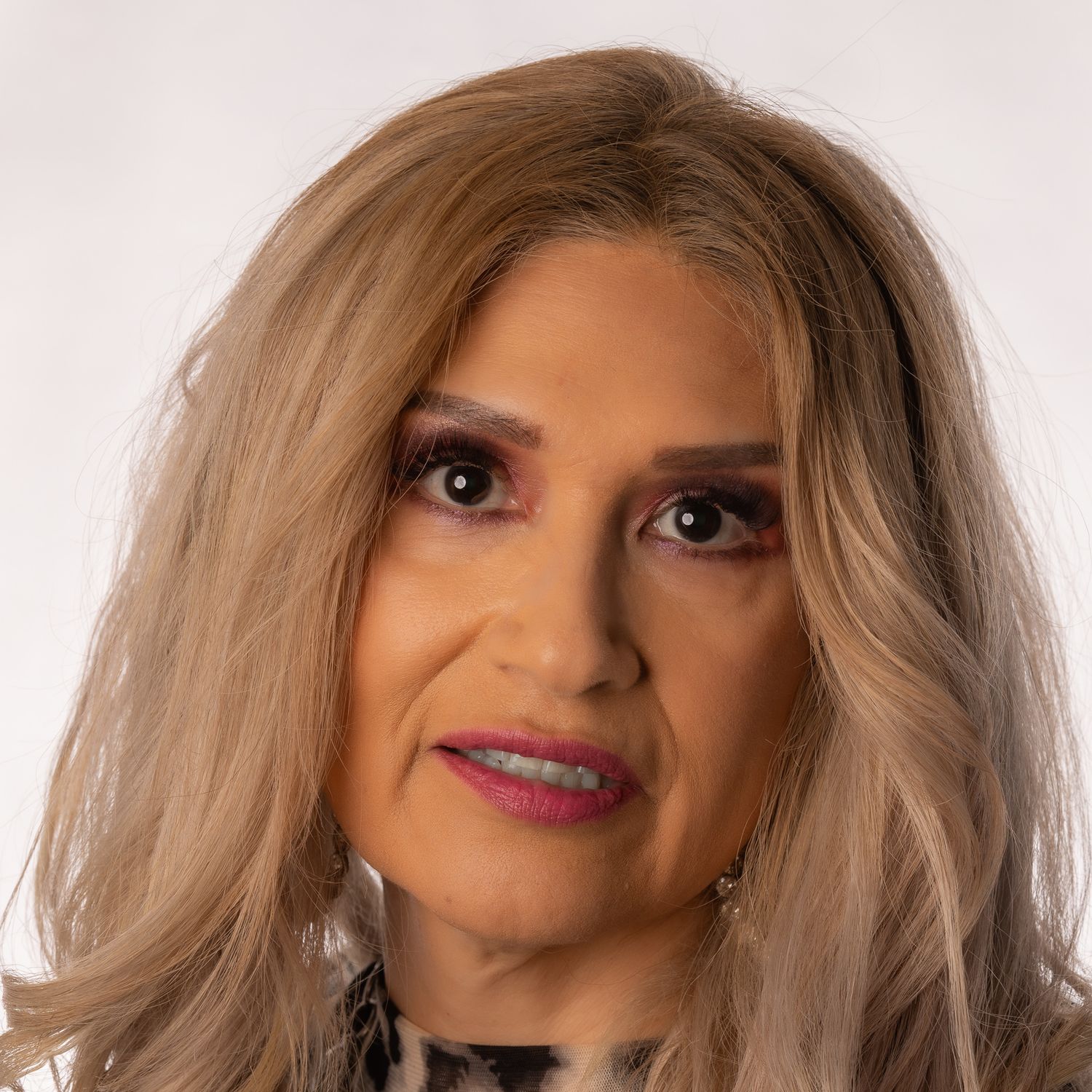 Professional headshot of a woman with blonde hair, bold pink lips, and elegant makeup against a light background.