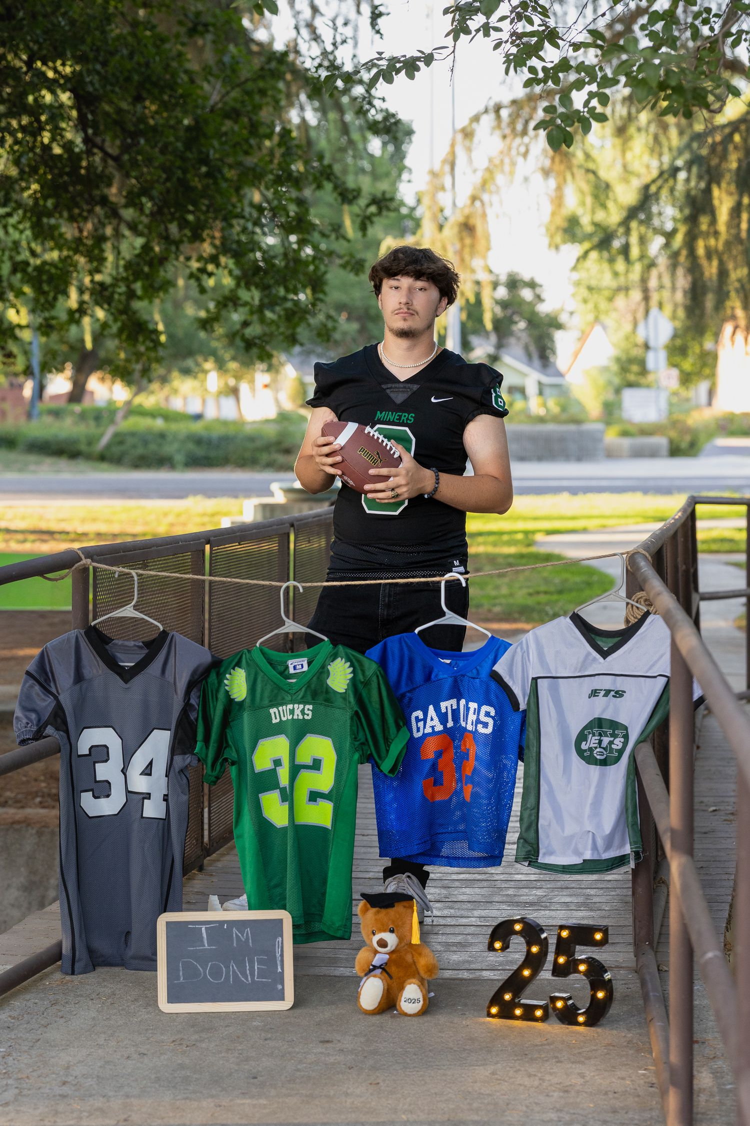 Senior football player holds a ball, displaying jerseys numbered 34, 32, 33, and a Jets jersey, with a sign reading I'm Done.
