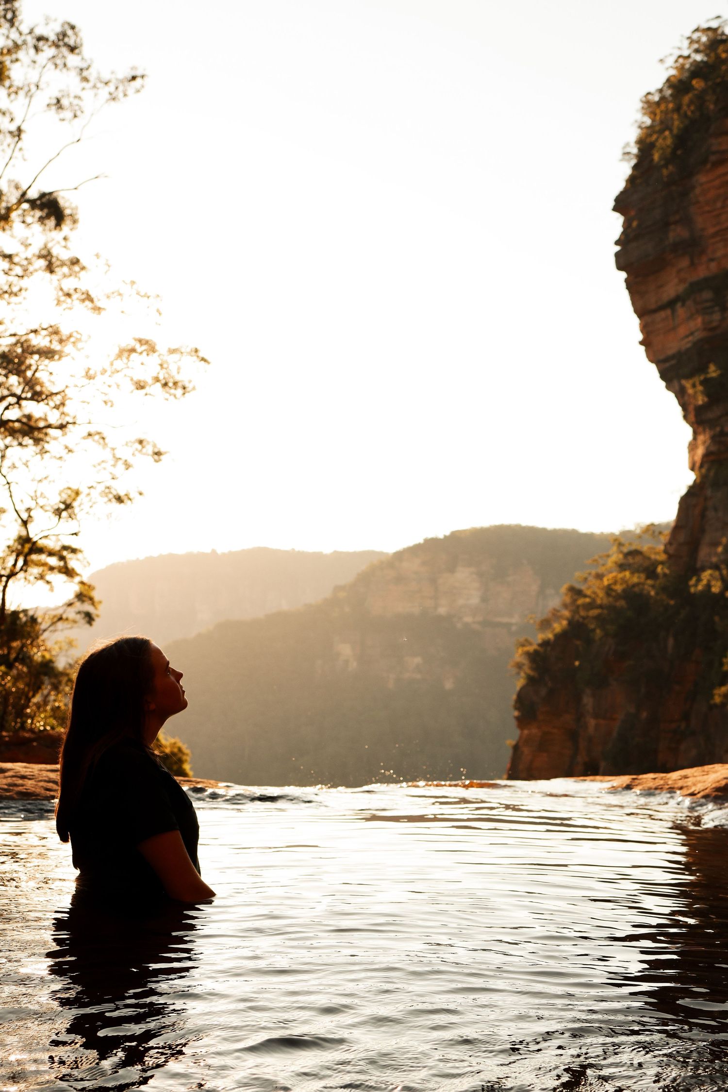 Silhouette at sunset in a natural mountain pool with dramatic cliff backdrop.