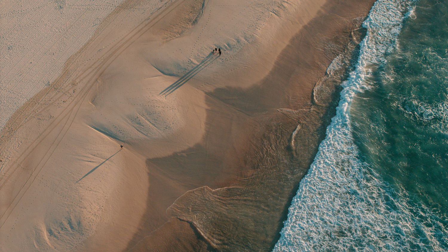 Aerial view of sandy beach shoreline with ocean waves and rippled sand patterns captured from above.