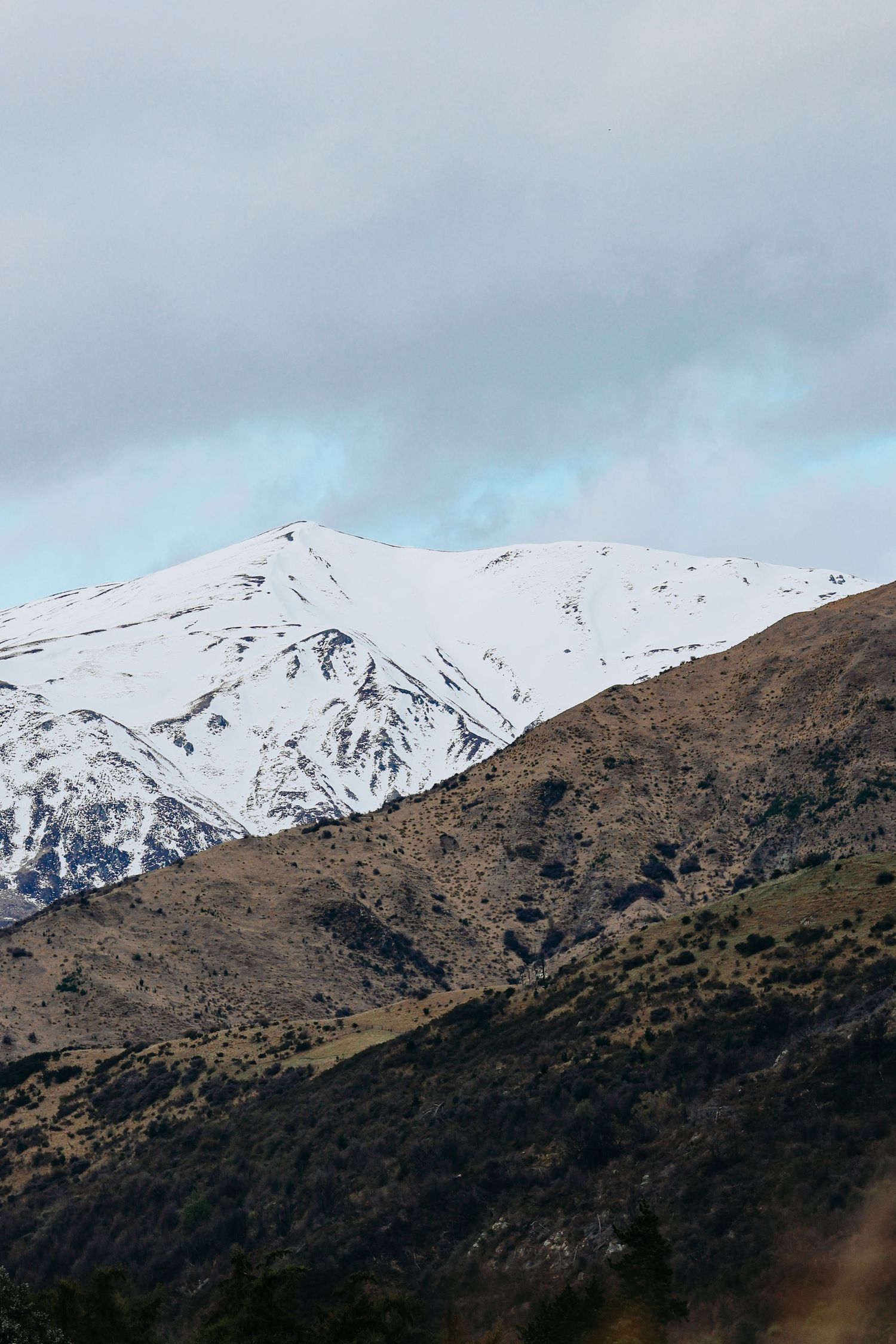 Snow-capped mountain peaks rising above dark foothills under cloudy skies.