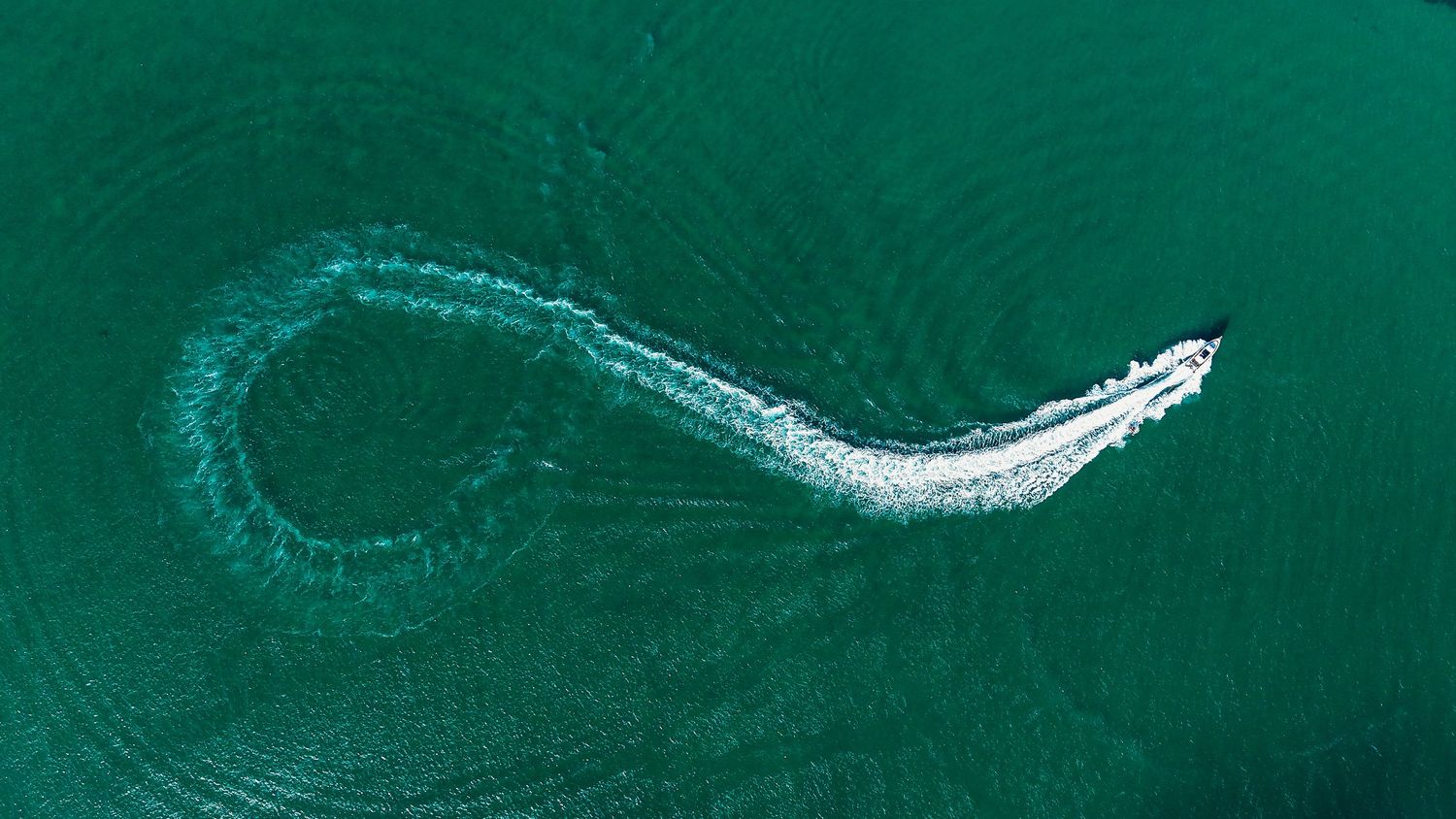 Curved wake pattern from boat cutting through deep emerald green ocean water.