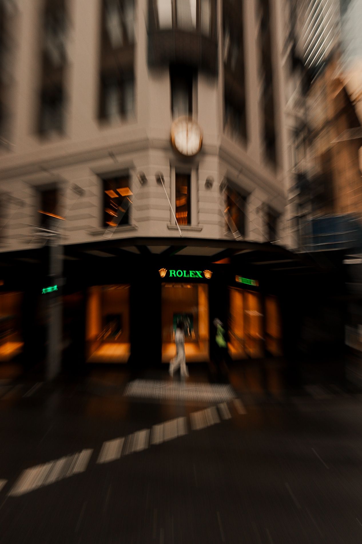 Blurred interior corridor of a luxury shopping mall with a Rolex store sign visible.