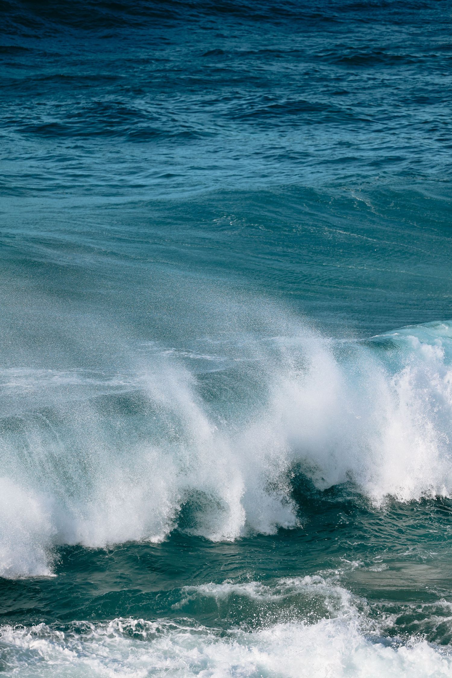 Powerful ocean waves crashing with white sea foam against deep blue turquoise water in the open sea.