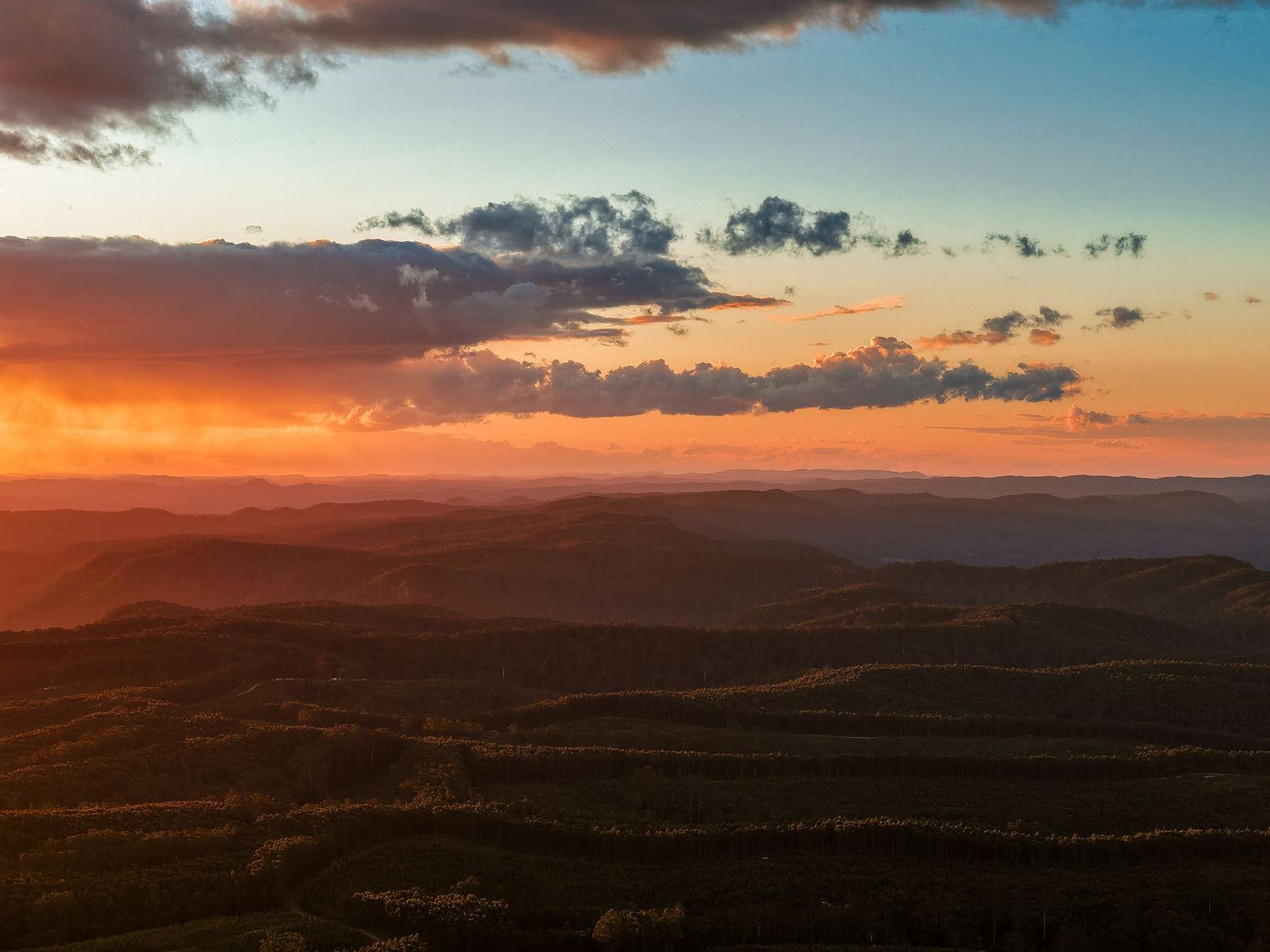 Rolling hills silhouetted against dramatic orange and purple sunset sky.