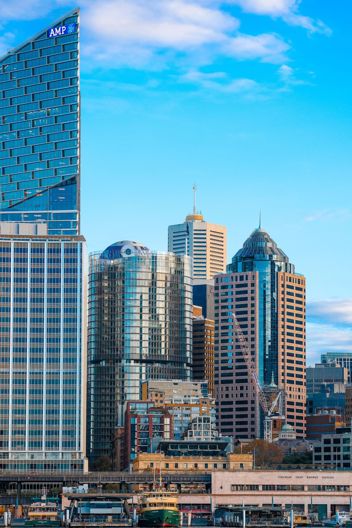 Modern glass skyscrapers and office buildings in downtown Sydney against bright blue sky.