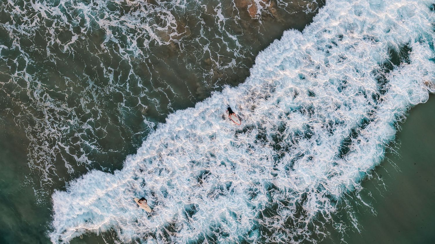 Dynamic aerial view of ocean waves creating white foam patterns against rocky shore.