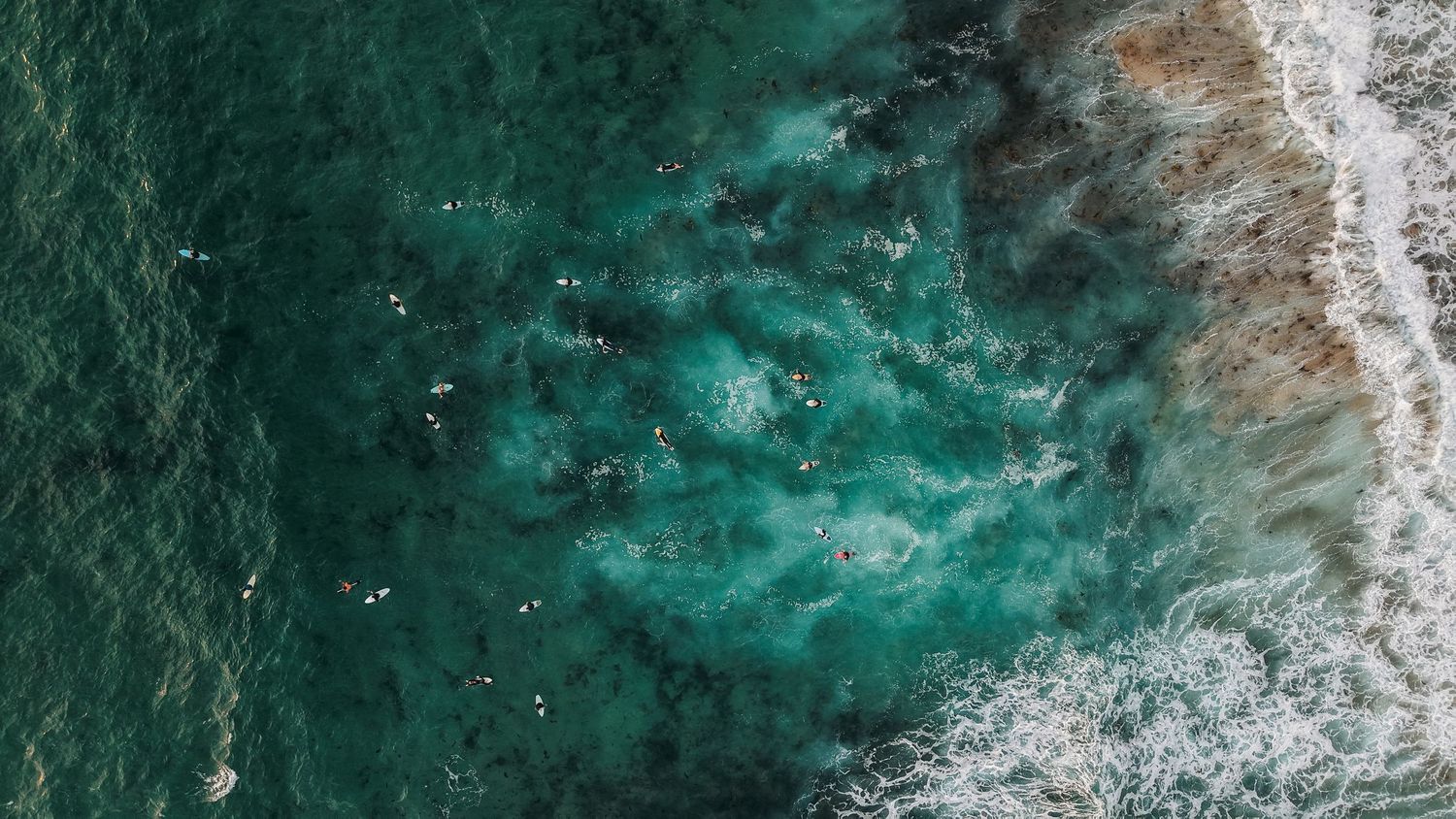 Aerial view of turquoise ocean waves crashing against a rocky coastline.