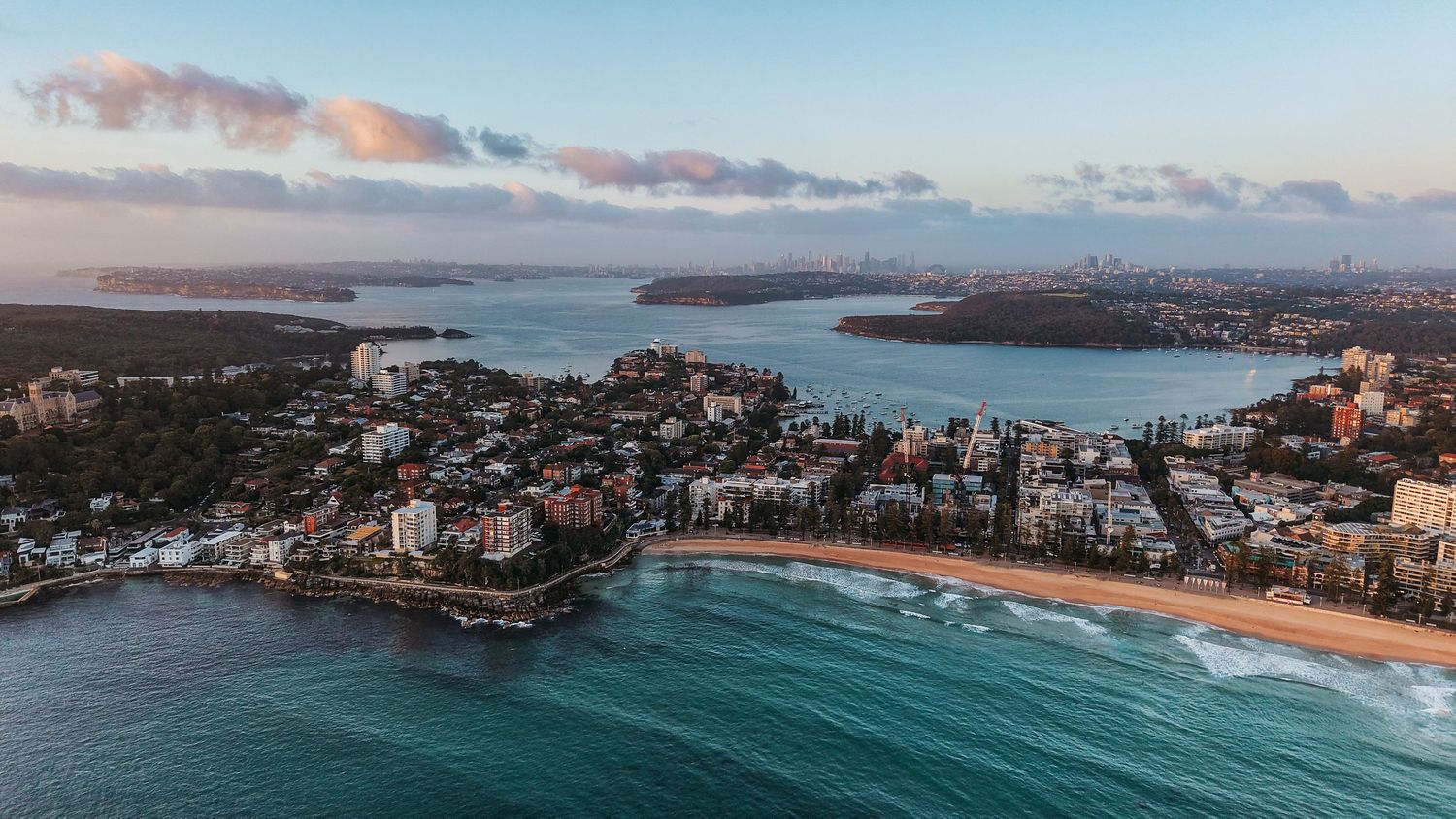 Panoramic coastal cityscape with beaches and buildings under sunset sky.