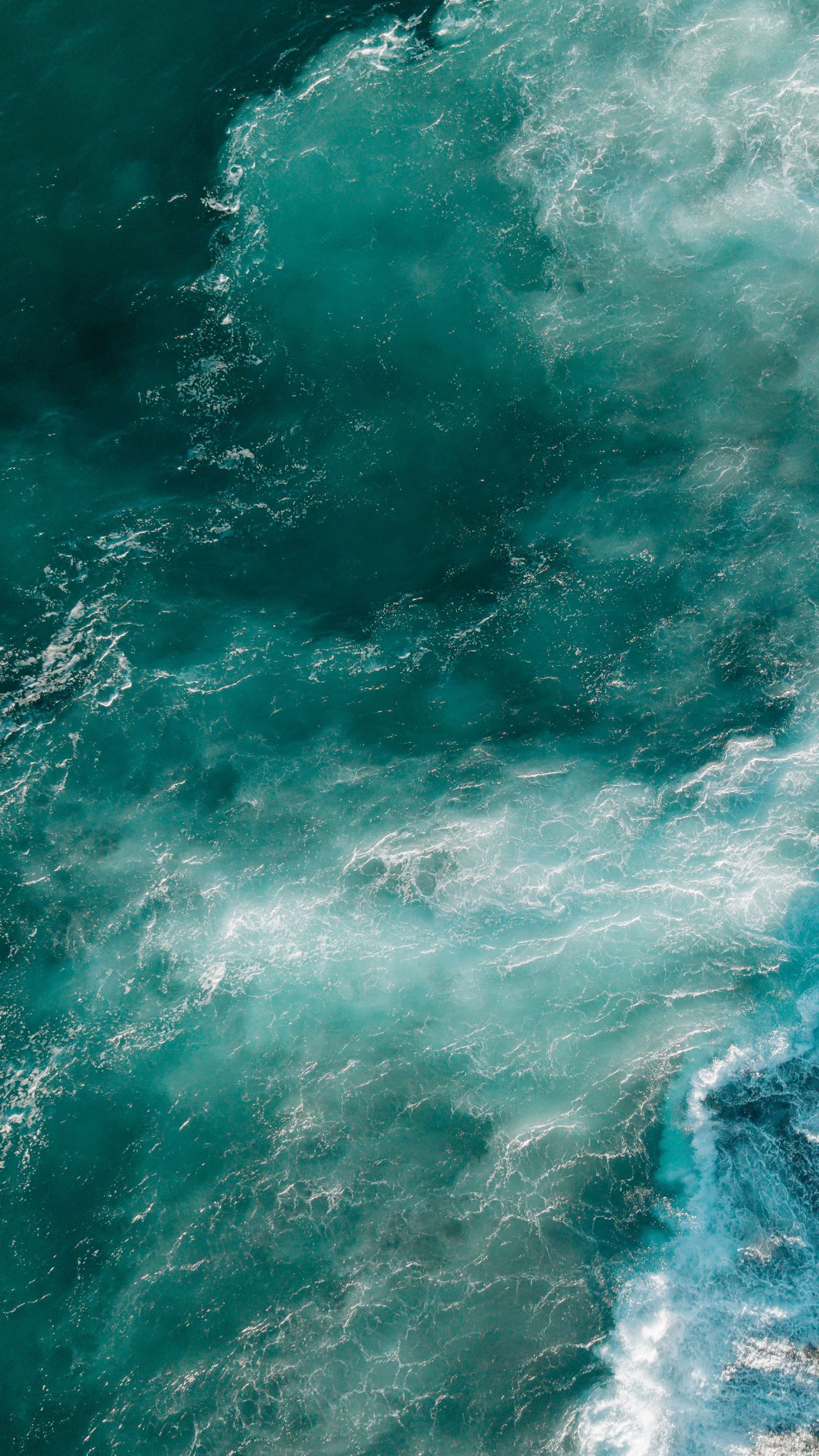 Aerial view of turquoise ocean waves with white sea foam creating abstract patterns.