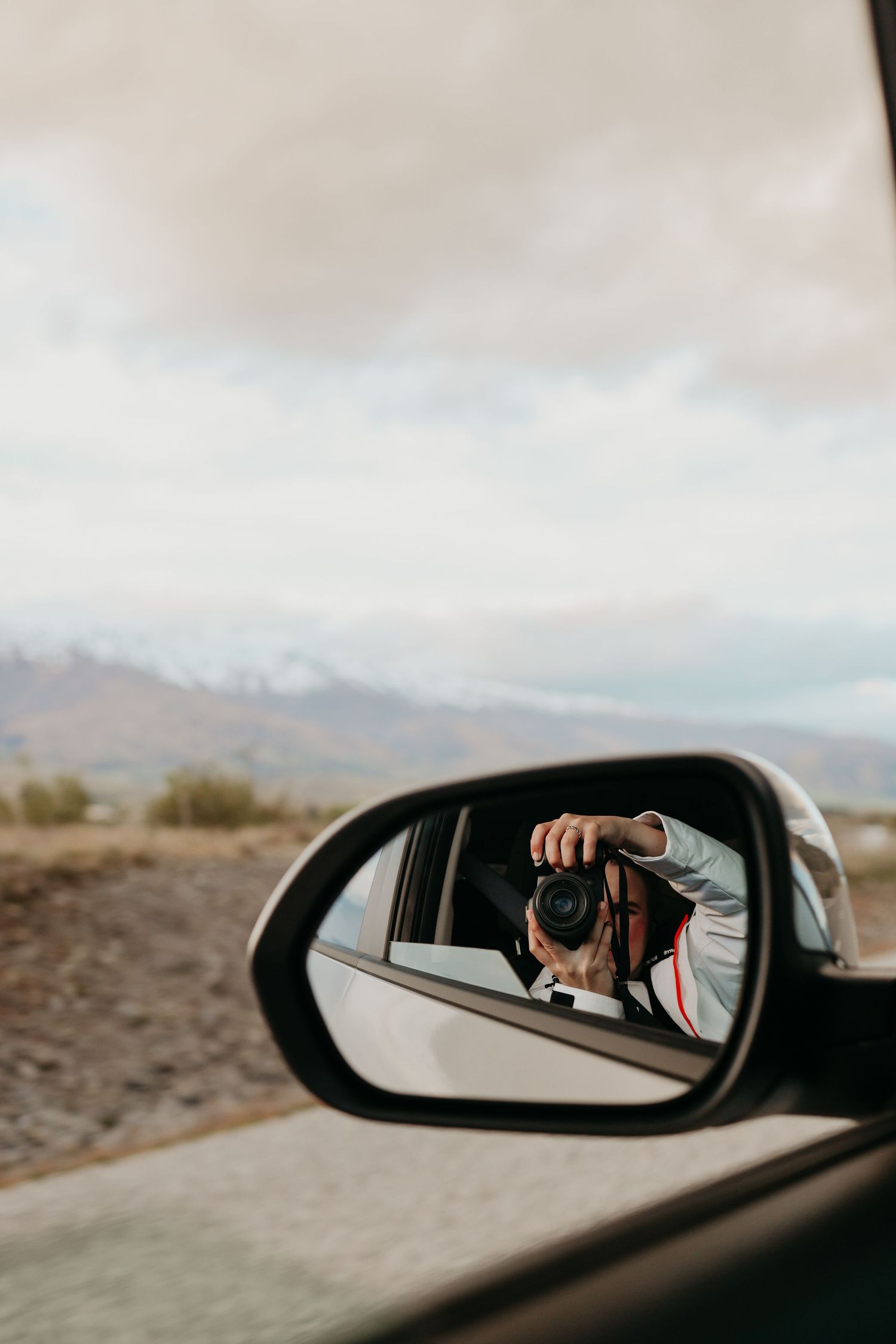 Camera reflection in car side mirror showing photography equipment against desert backdrop.