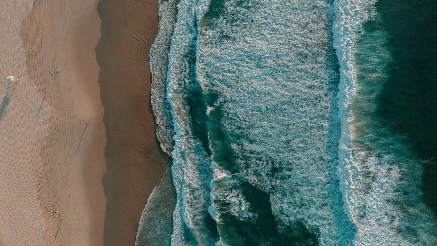 Aerial drone view of turquoise ocean waves washing onto a sandy beach shoreline.