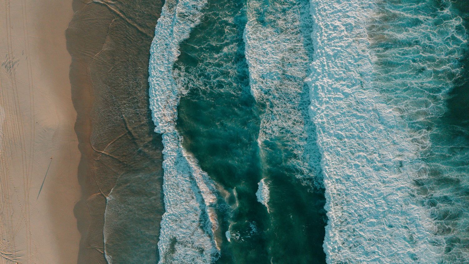Aerial view of turquoise ocean waves crashing onto a sandy beach shore.