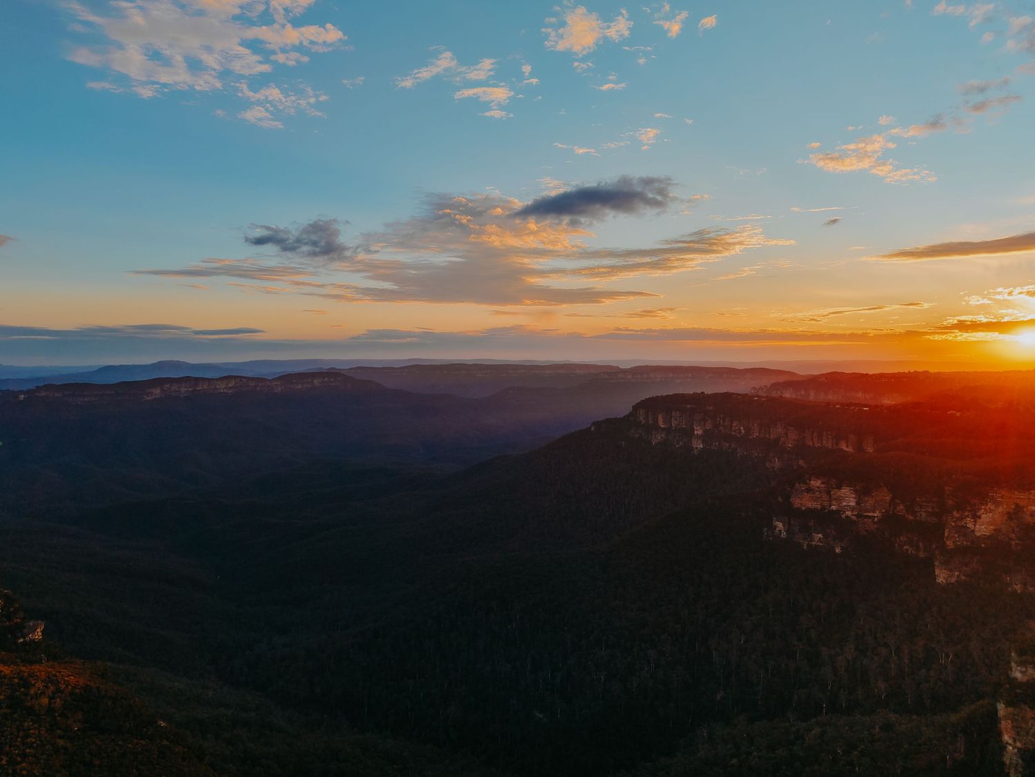 Dramatic mountain sunset with golden light illuminating clouds over rocky cliffs.