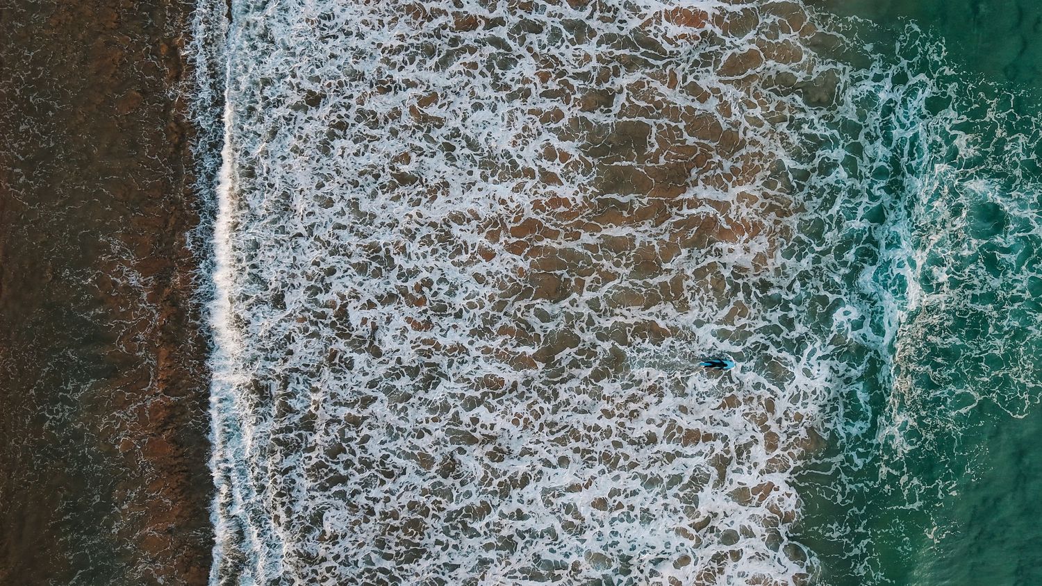 Close-up aerial view of white ocean waves crashing against turquoise waters.