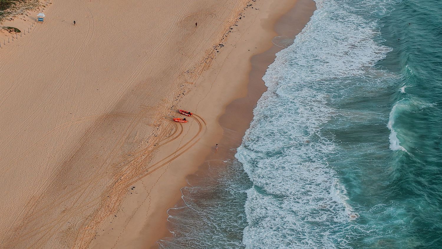 Aerial shot of pristine beach where turquoise waters meet golden sand along the shoreline.