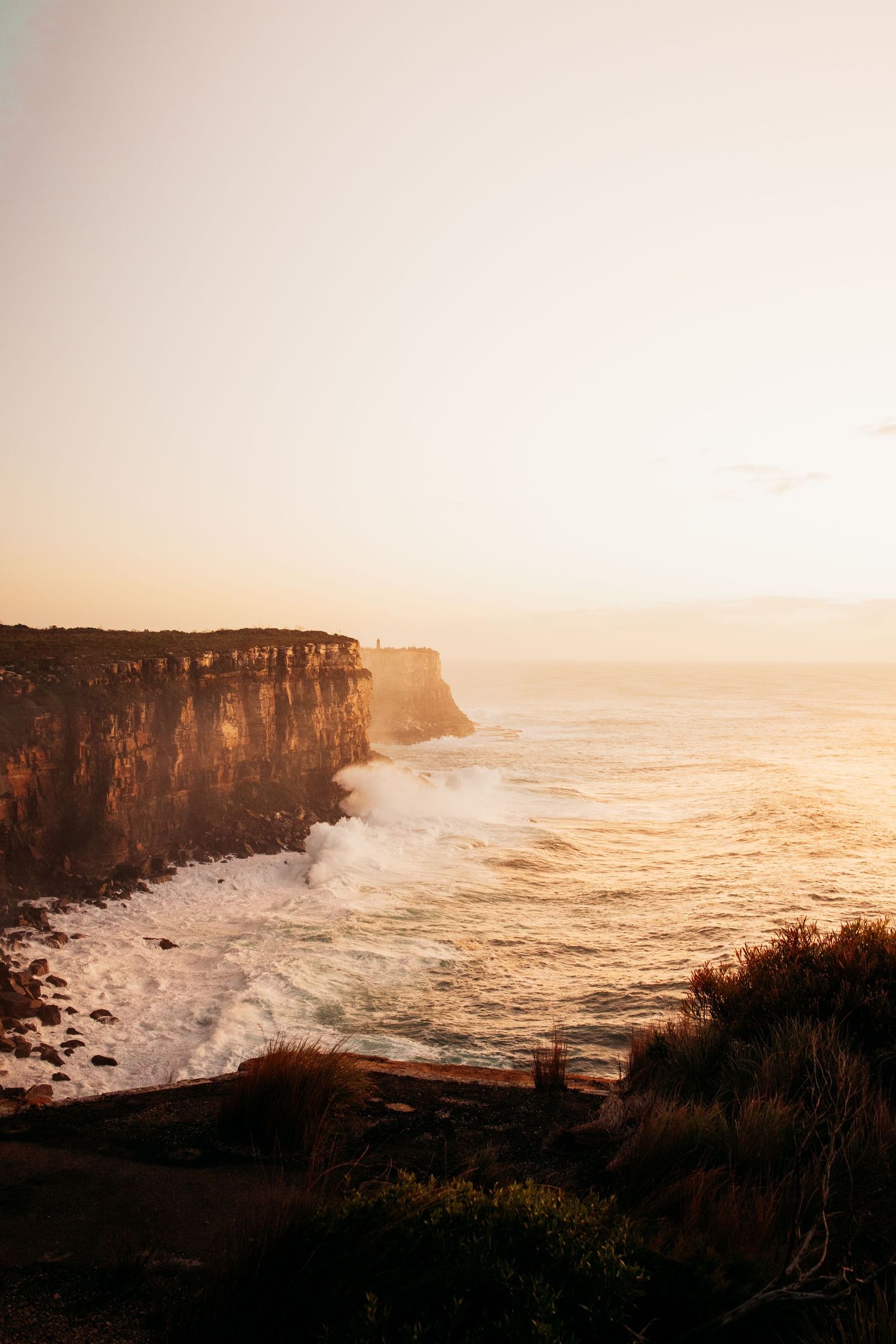 Dramatic coastal cliffs at sunset with waves crashing against rocky shoreline.