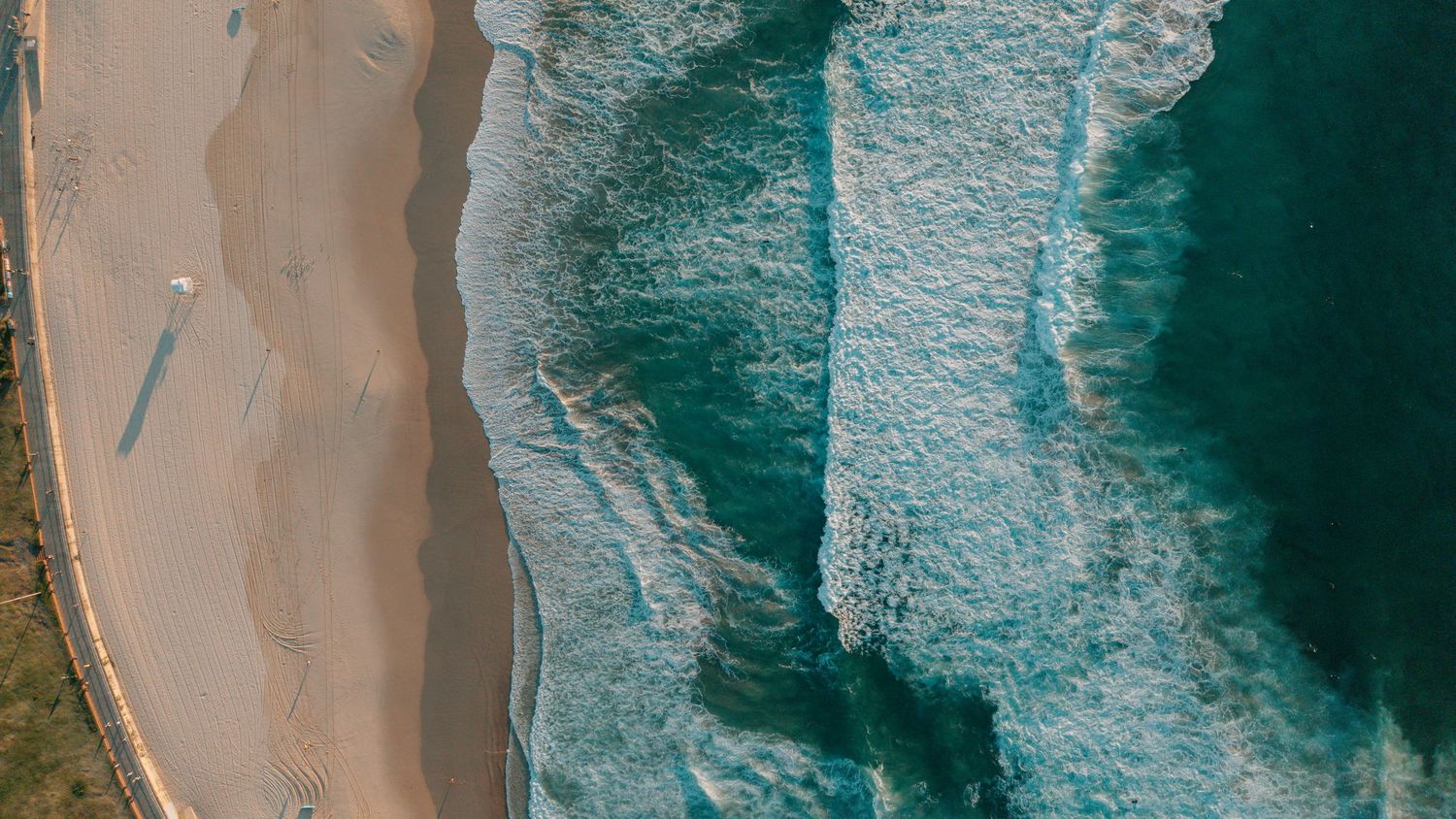 Aerial view of turquoise ocean waves crashing onto a sandy beach shoreline captured from above.