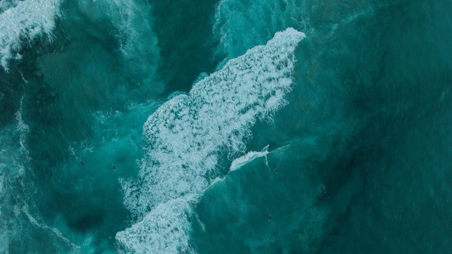 Aerial view of turquoise ocean waves with white sea foam and a surfer riding the surf.