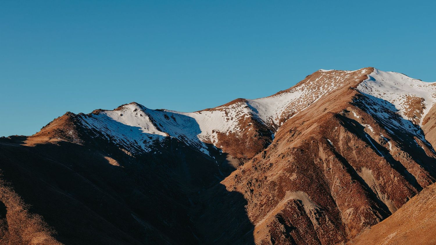 Panoramic mountain range silhouette against clear blue sky at sunrise.