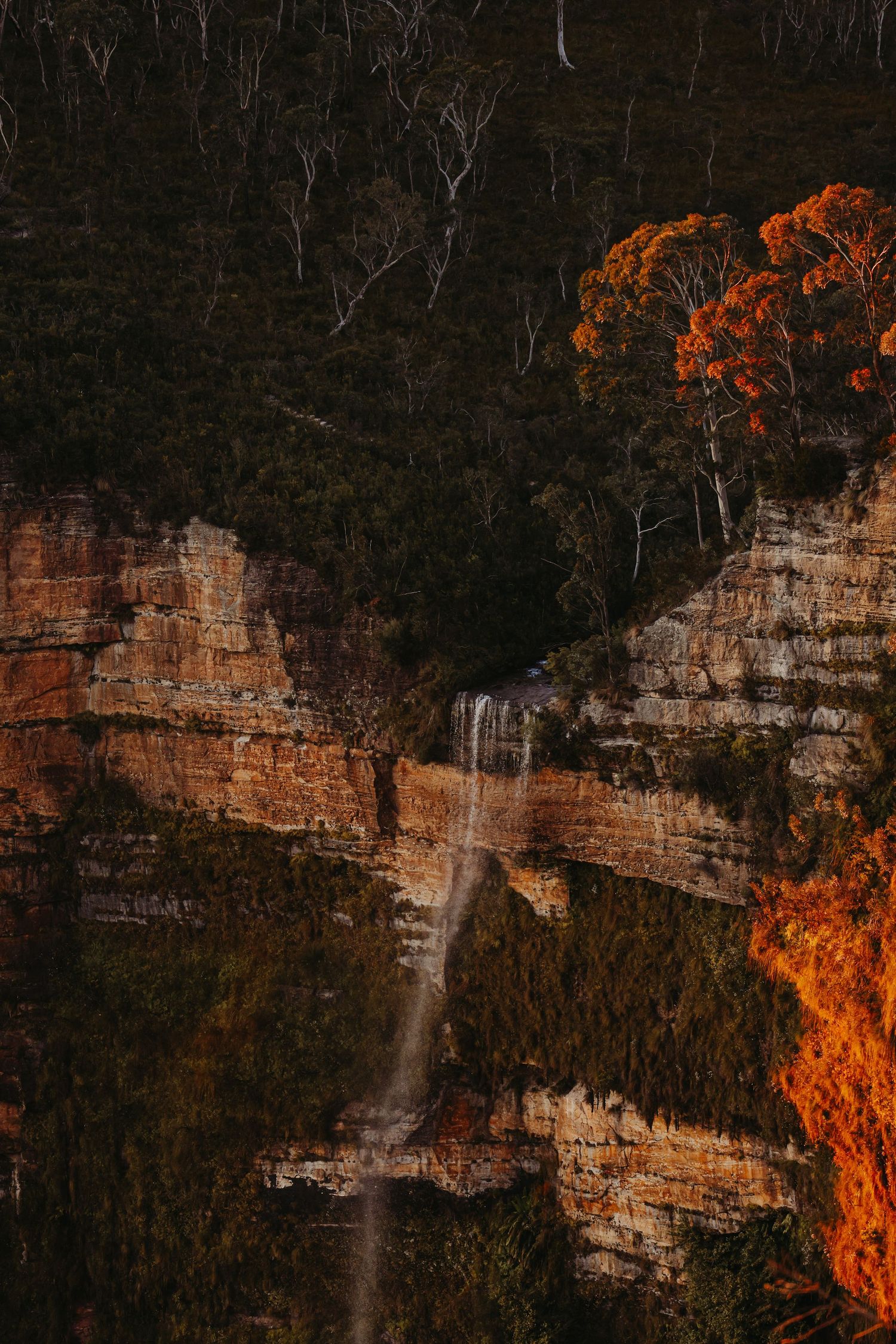 Majestic waterfall cascades down sandstone cliffs in golden morning light.
