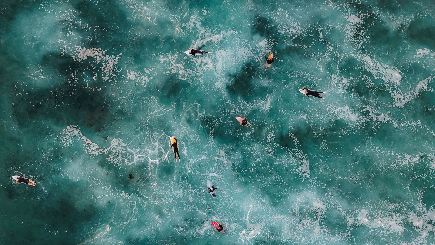 Aerial perspective of surfers riding waves in crystal clear turquoise waters near the beach.