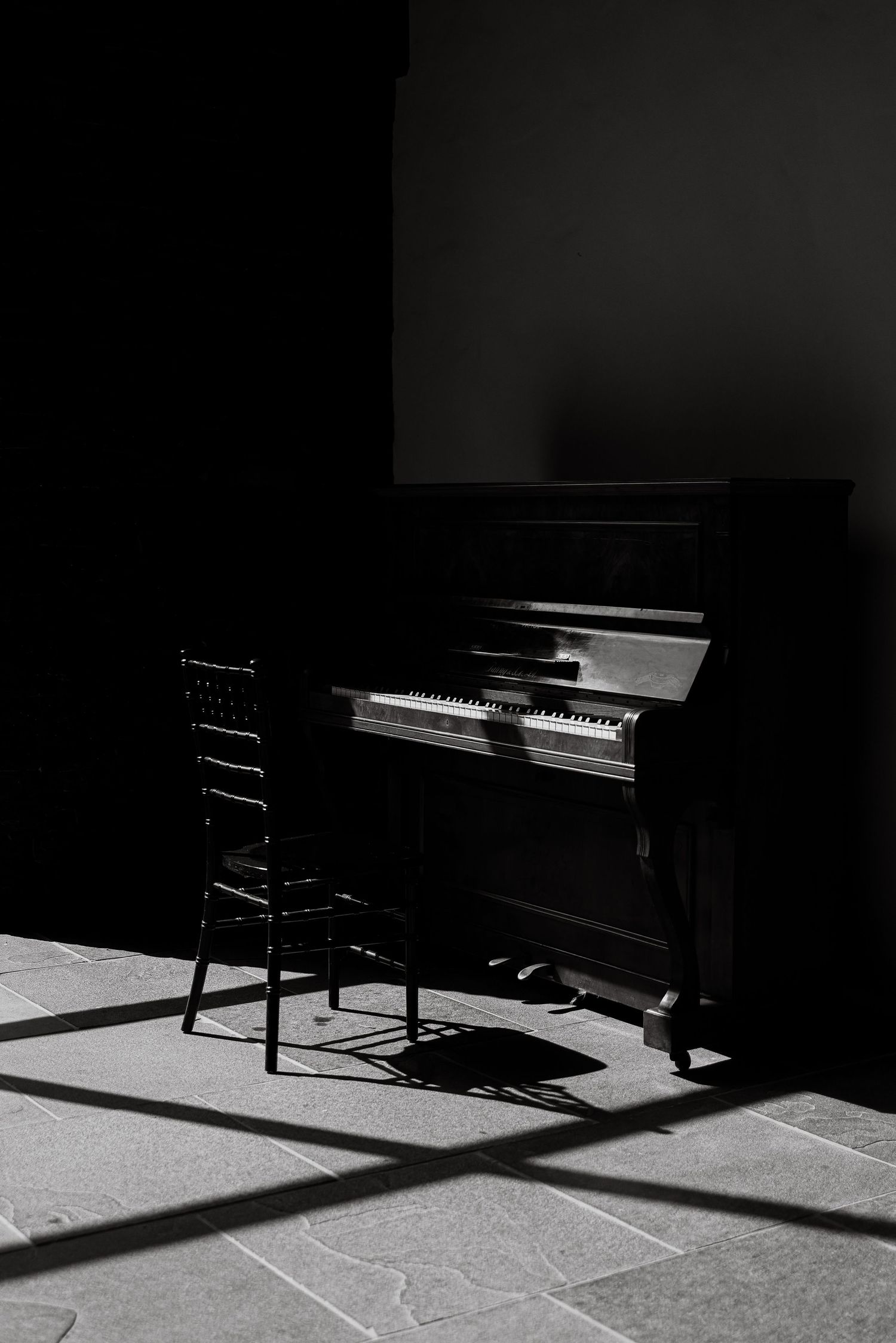 Dramatic black and white photo of piano and chair casting long shadows.