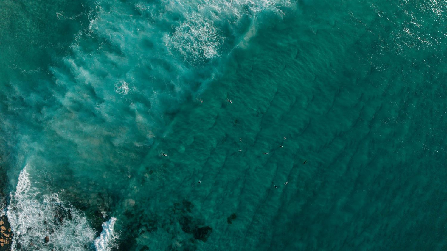 Aerial view of turquoise ocean waves crashing on rocky shore with white sea foam patterns.