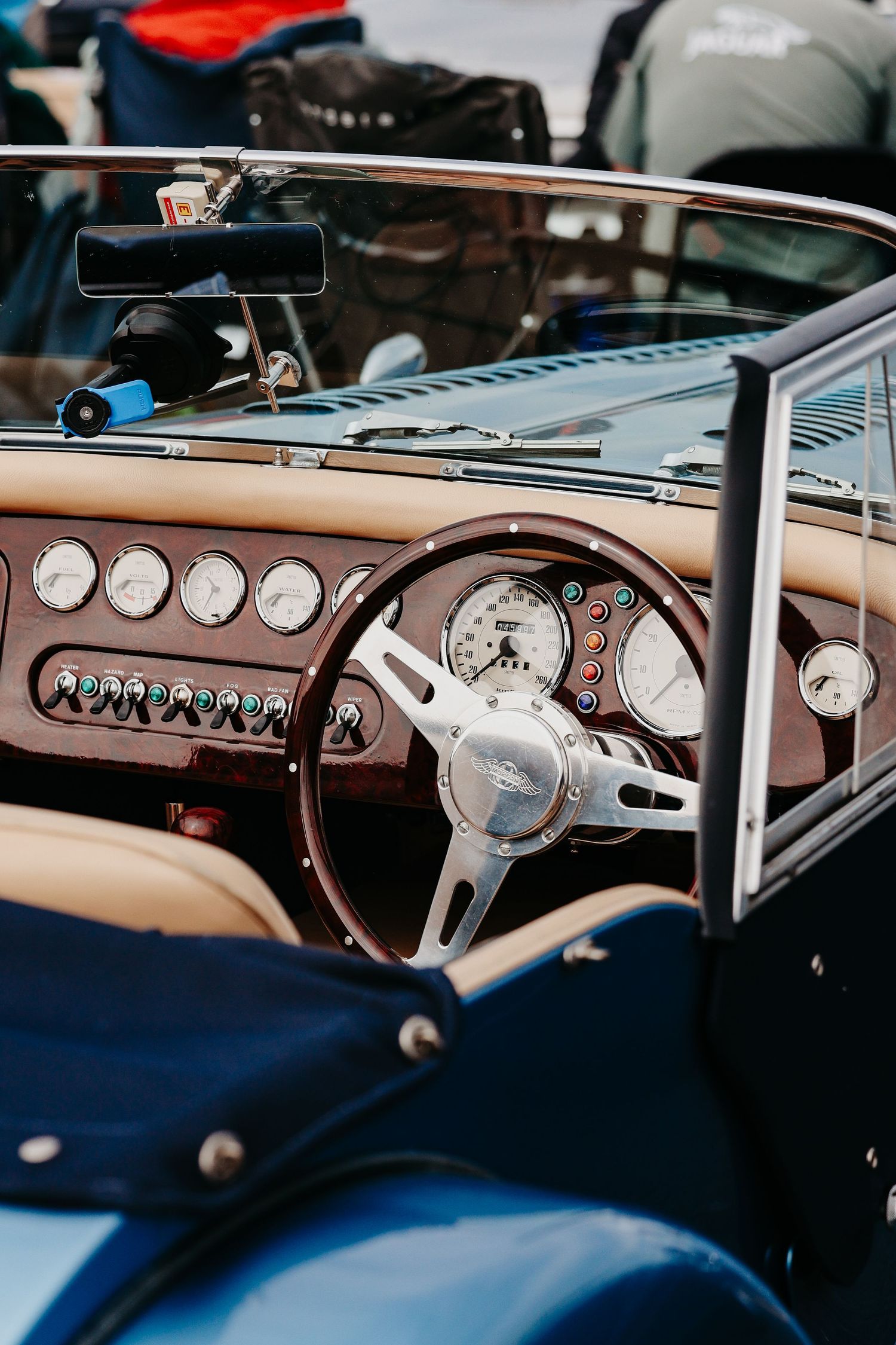 Vintage classic car interior with wooden steering wheel, leather seats, and retro dashboard gauges in a blue convertible.