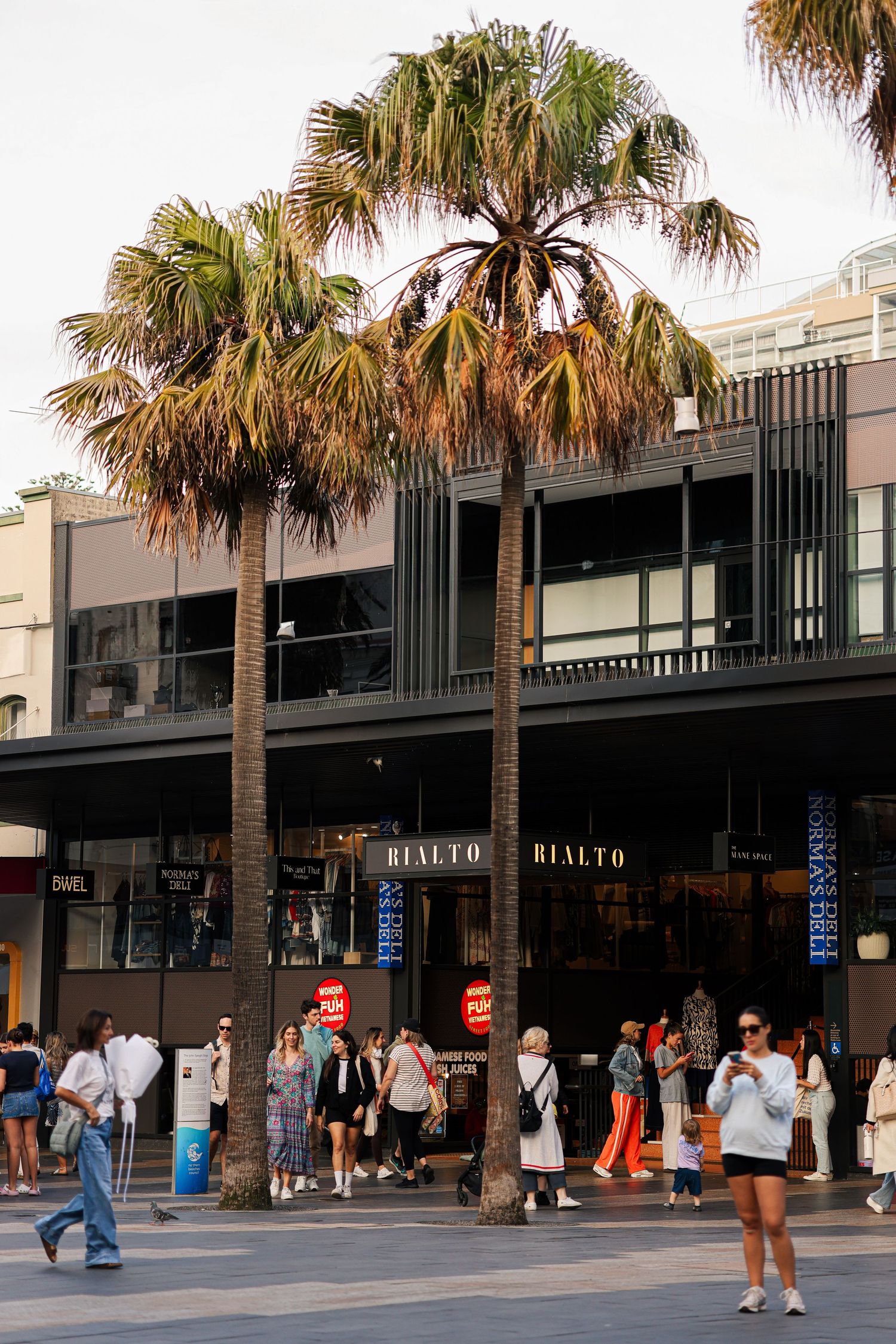Palm trees line the entrance of the Rialto shopping area with people walking by.