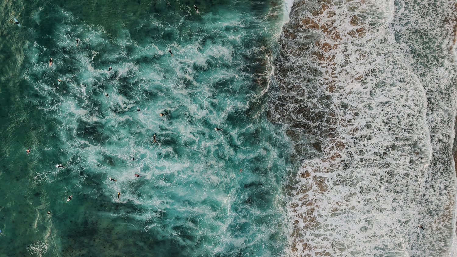 Abstract aerial view of turquoise ocean waves creating dynamic white foam patterns.