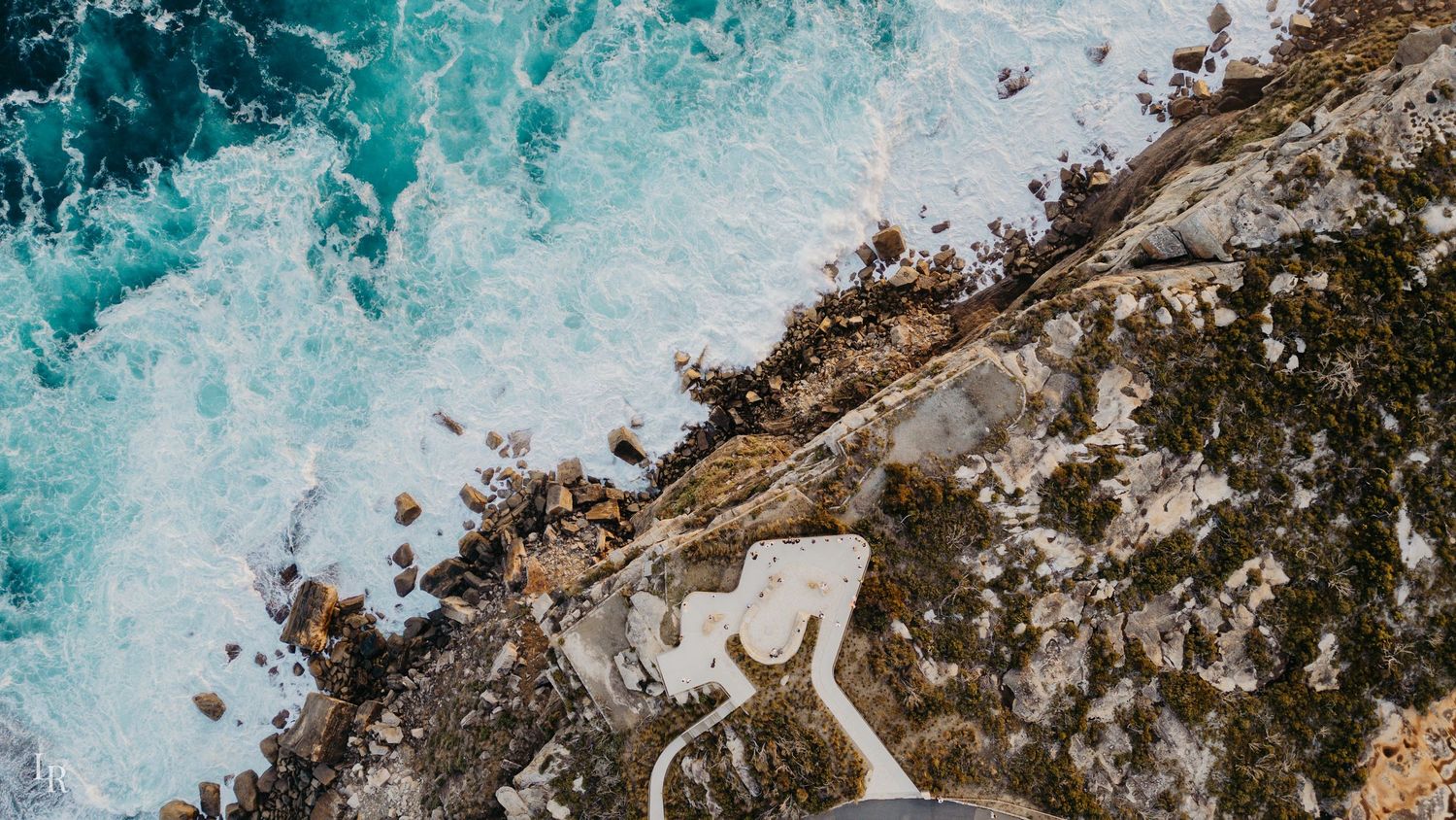 Turquoise ocean waves crashing against rugged coastal rocks creating white foam patterns.