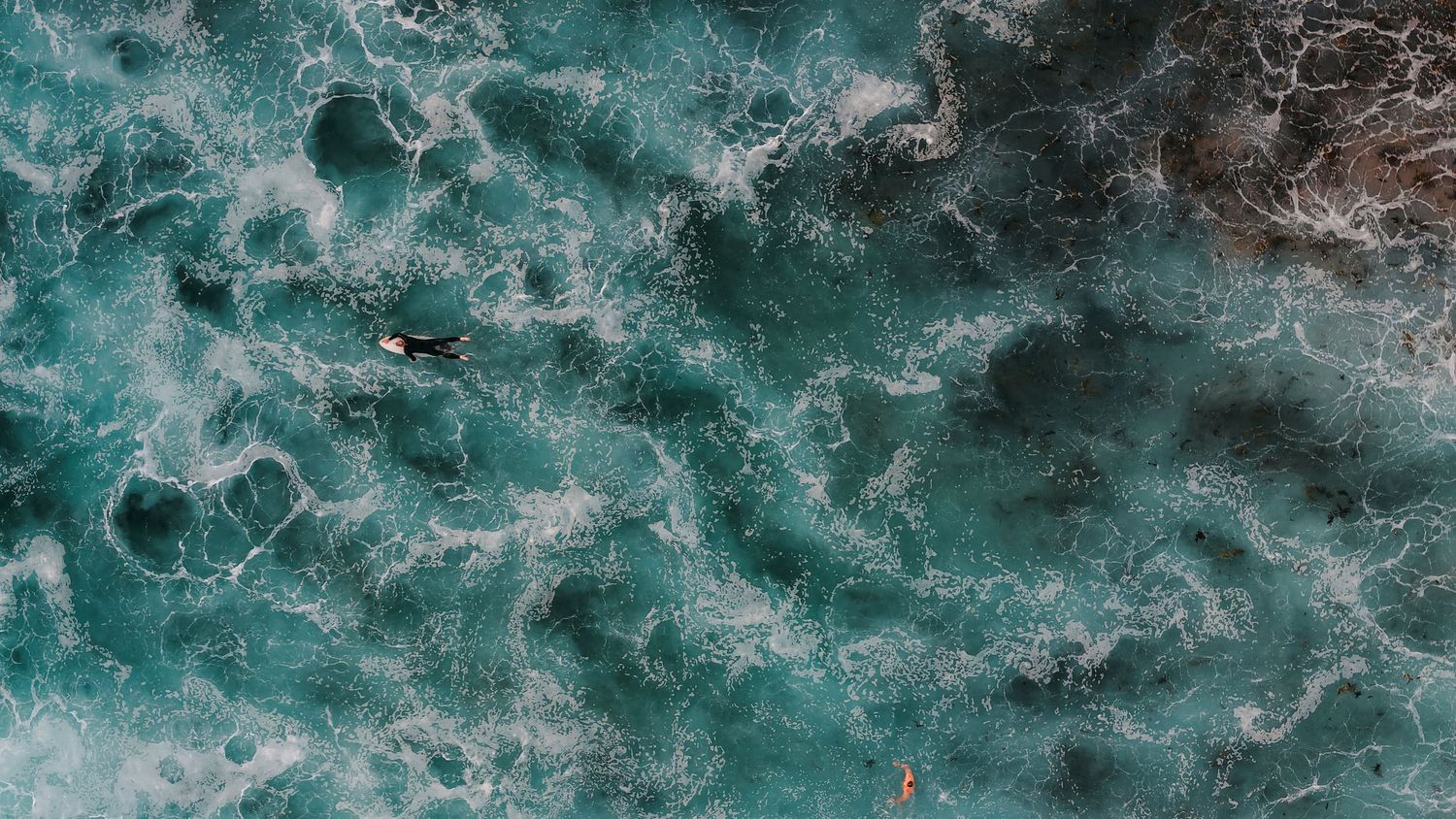 Aerial view of turquoise ocean waves crashing against a sandy beach creating dramatic patterns.