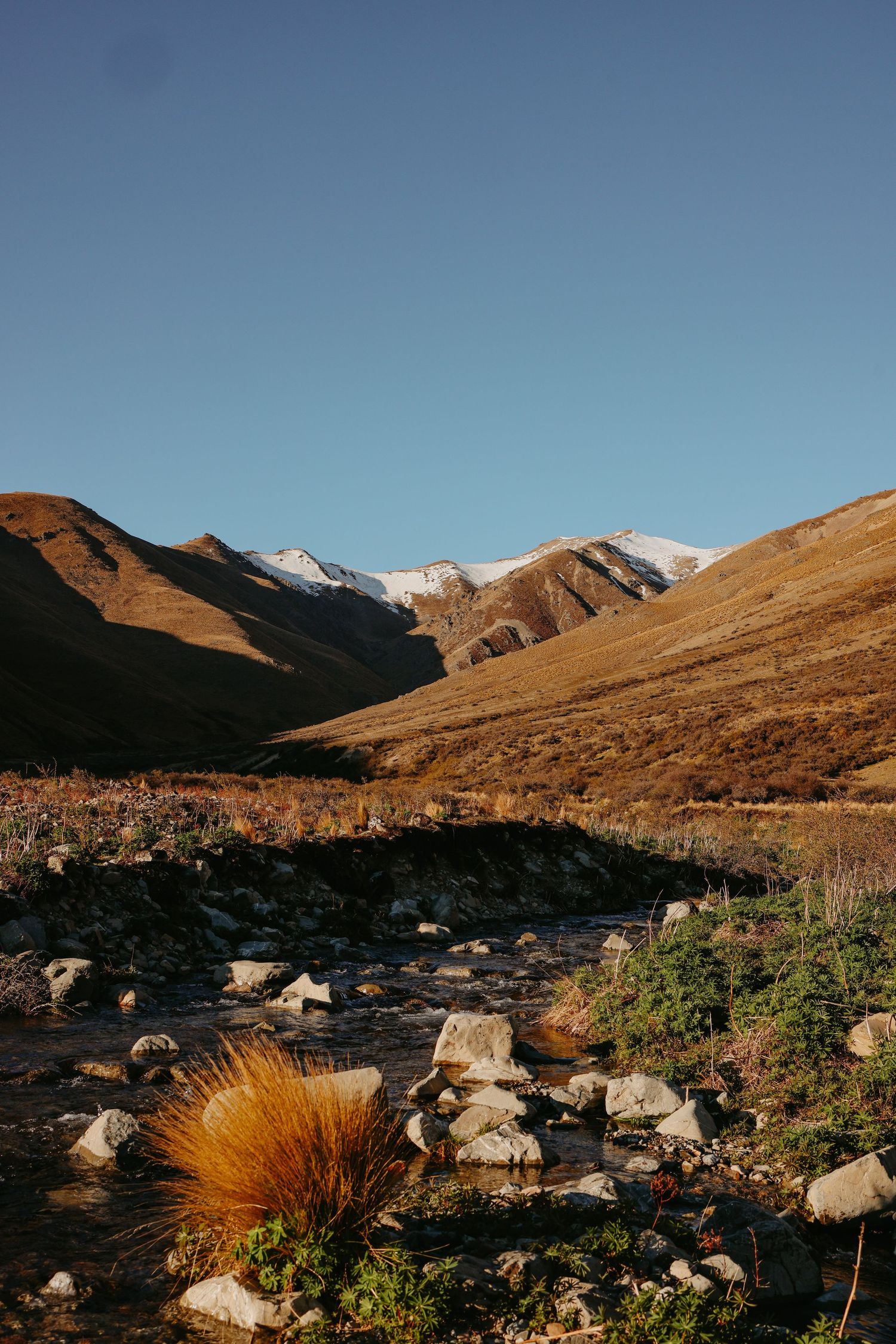 Rocky mountain landscape with snow-capped peaks and desert brush in the foreground.