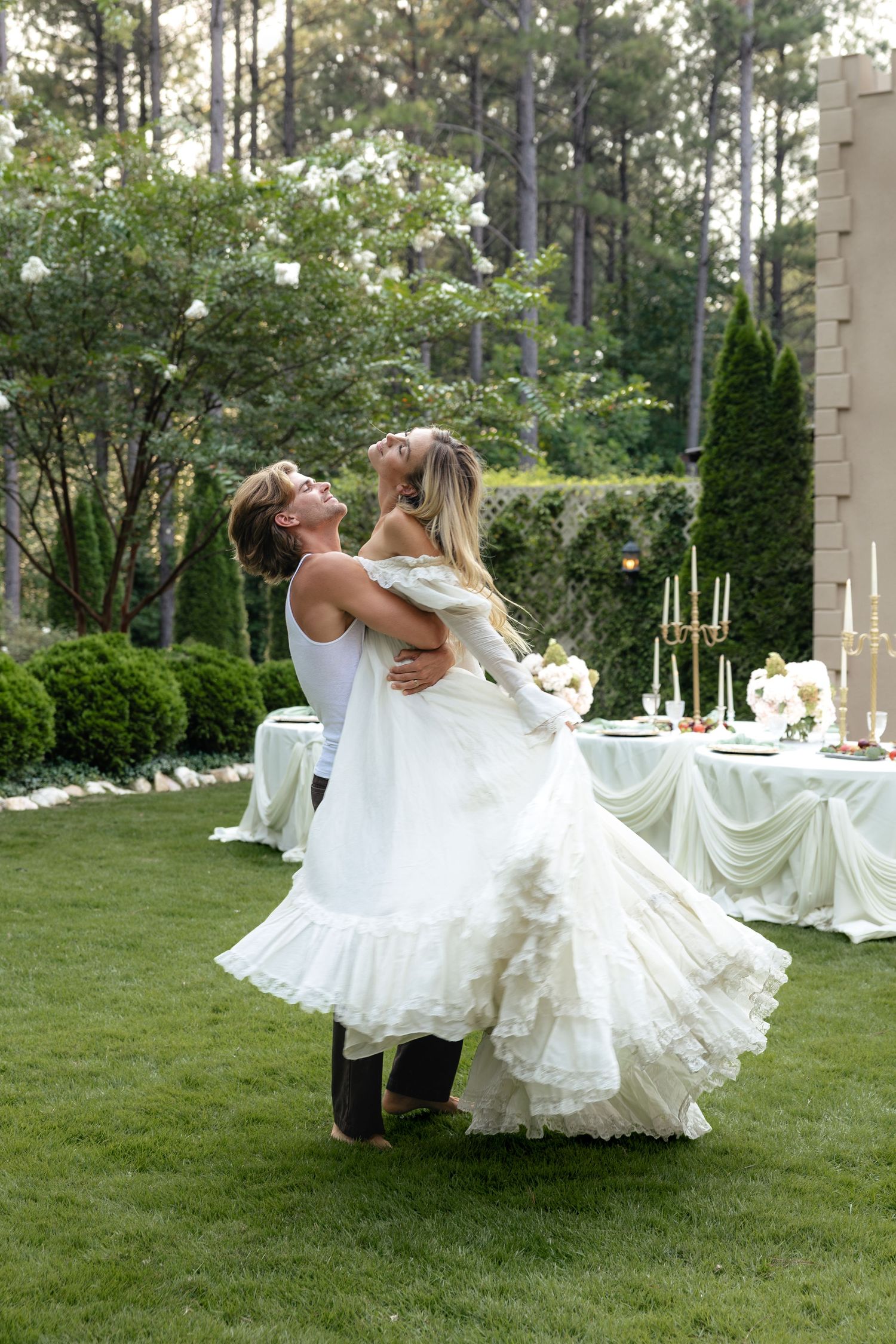 Groom lifting bride in a flowing white dress during outdoor garden wedding celebration.