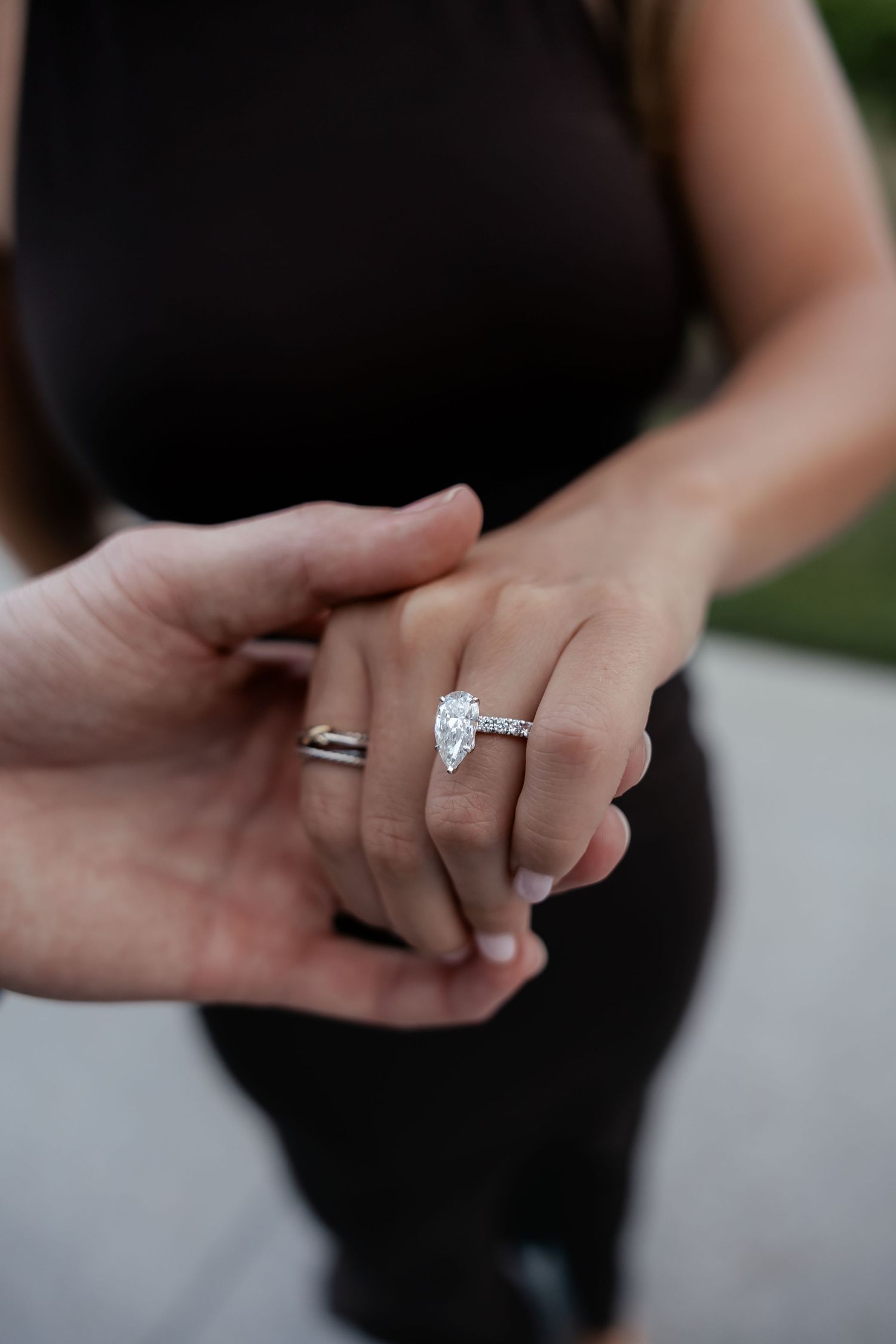 Close-up of a pear-shaped diamond engagement ring on a woman's hand held by a man.