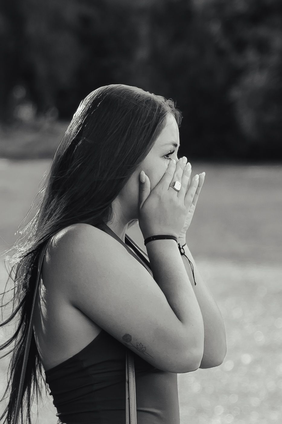 Black and white portrait of emotional woman with long hair covering face with hands outdoors.