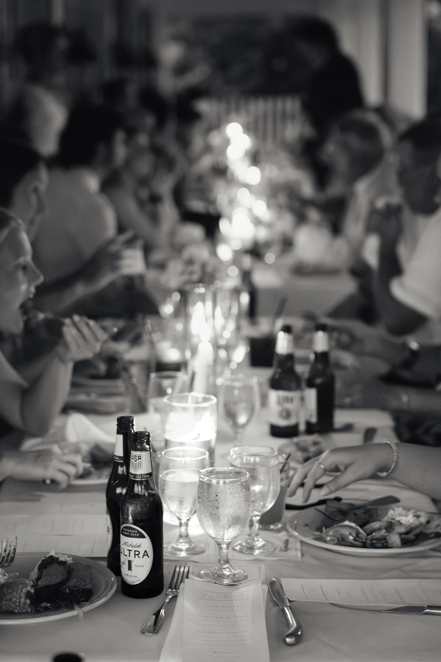 Black and white photo of guests dining at a long table with Michelob Ultra bottles, wine glasses, and candles.