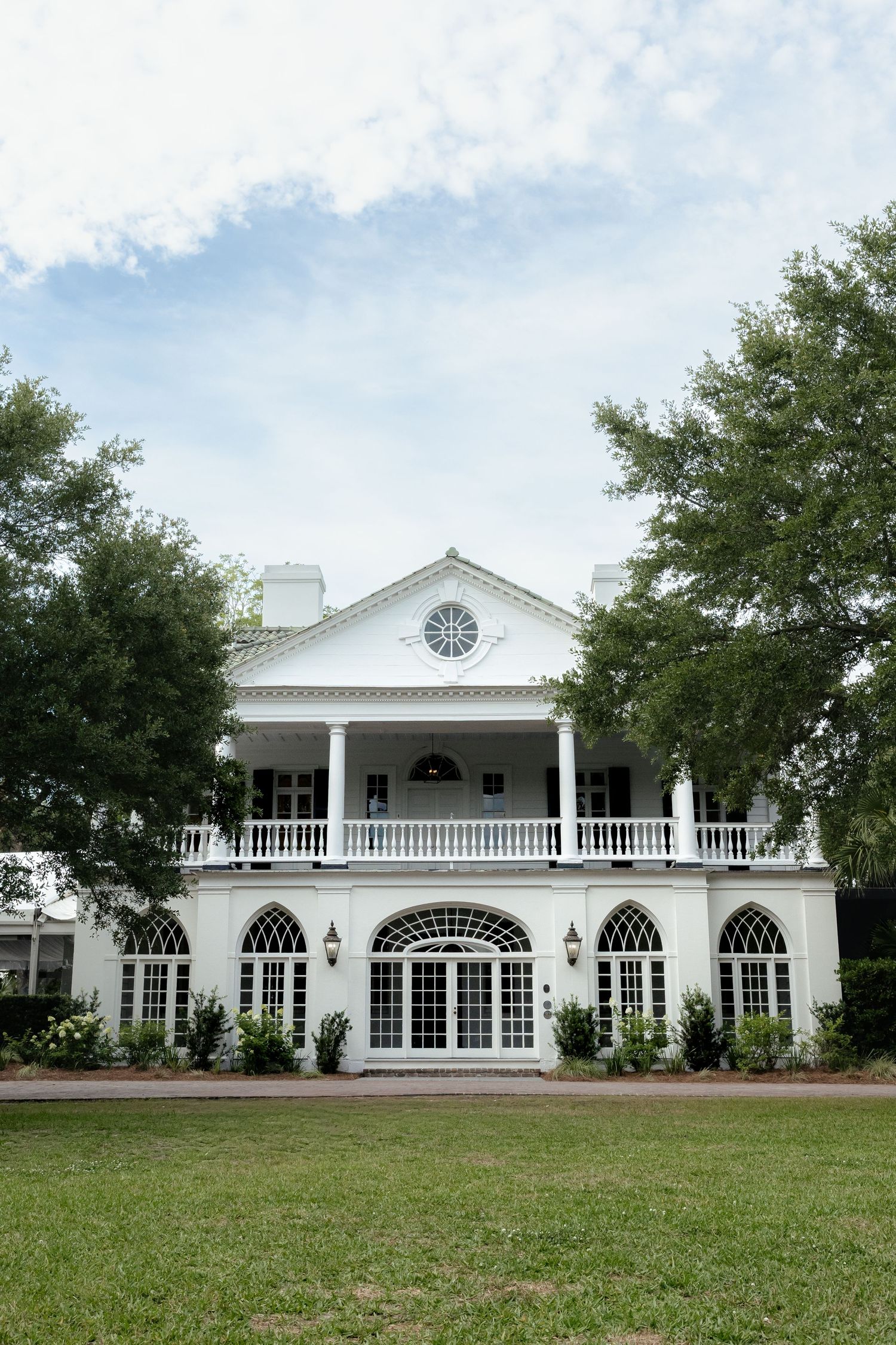 Elegant white two-story Southern mansion with balcony and arched windows surrounded by trees.