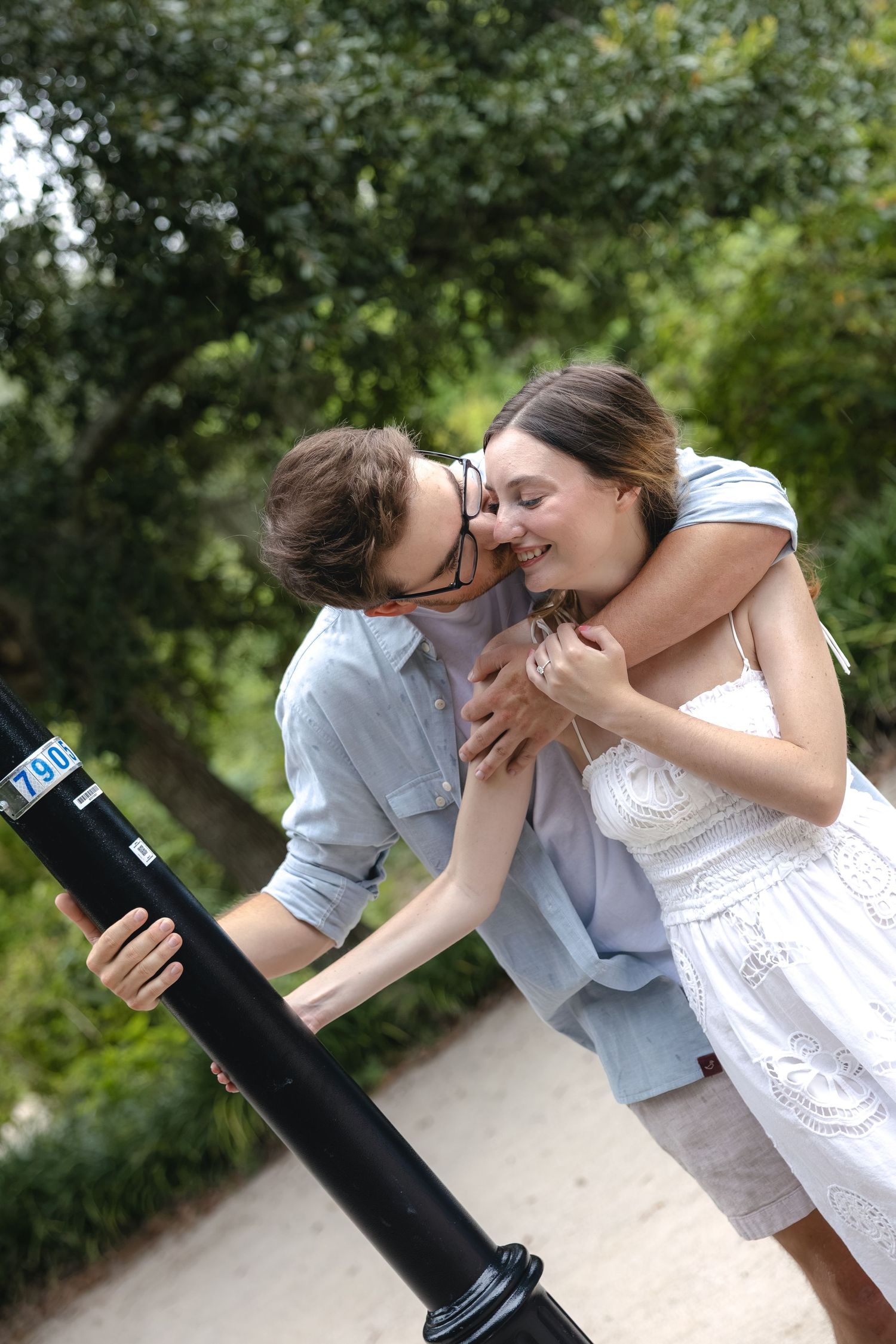 A young couple sharing a tender moment outdoors, laughing together near a black pole in a lush green park.