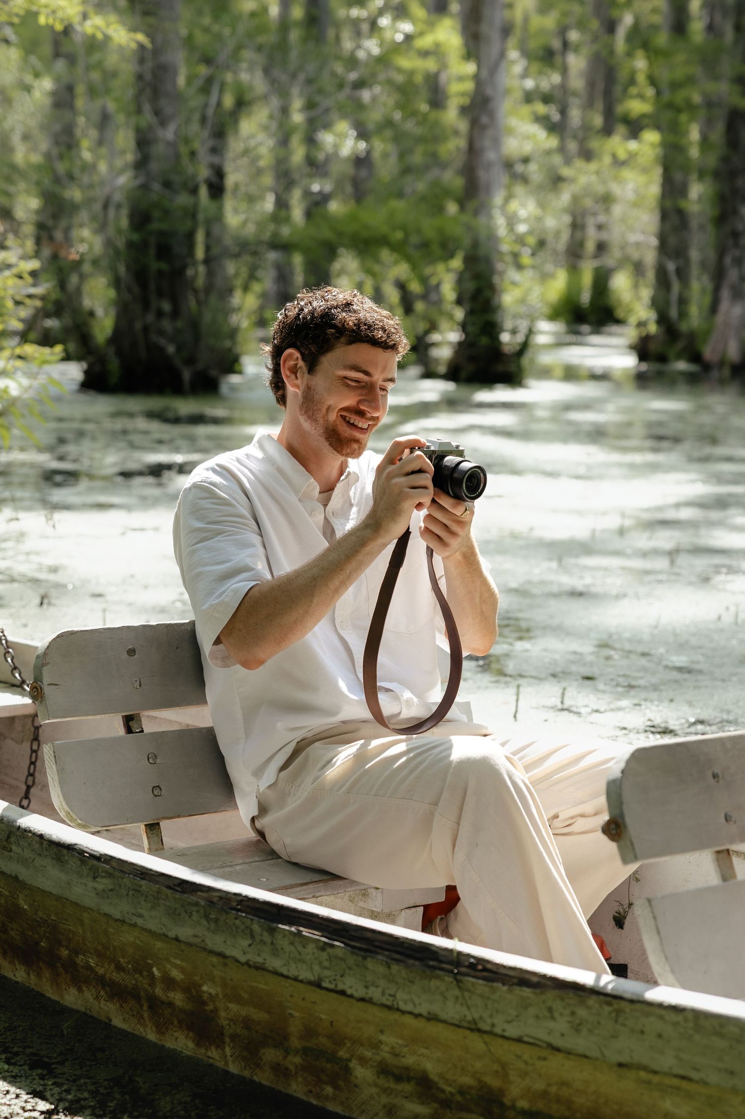Smiling man sitting in a rowboat on a swamp, reviewing photos on a vintage film camera.