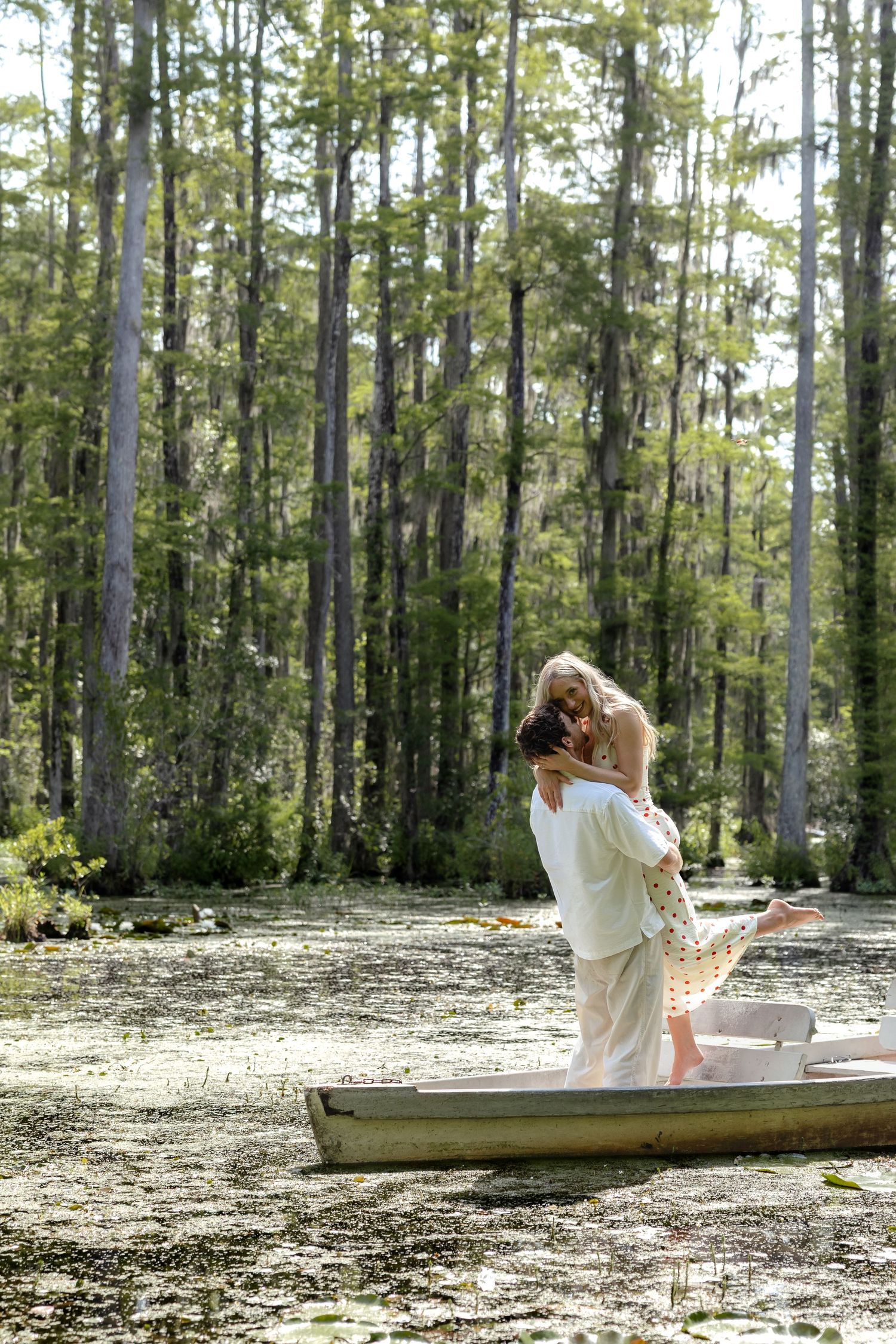 Man lifting woman in a romantic embrace while standing in a rowboat on a cypress swamp.