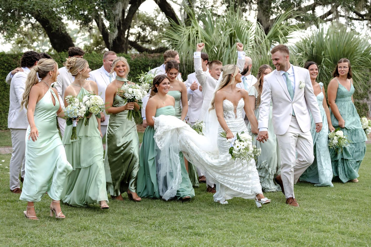 Joyful wedding party walks outdoors, bridesmaids in mint green gowns with groomsmen in light suits.